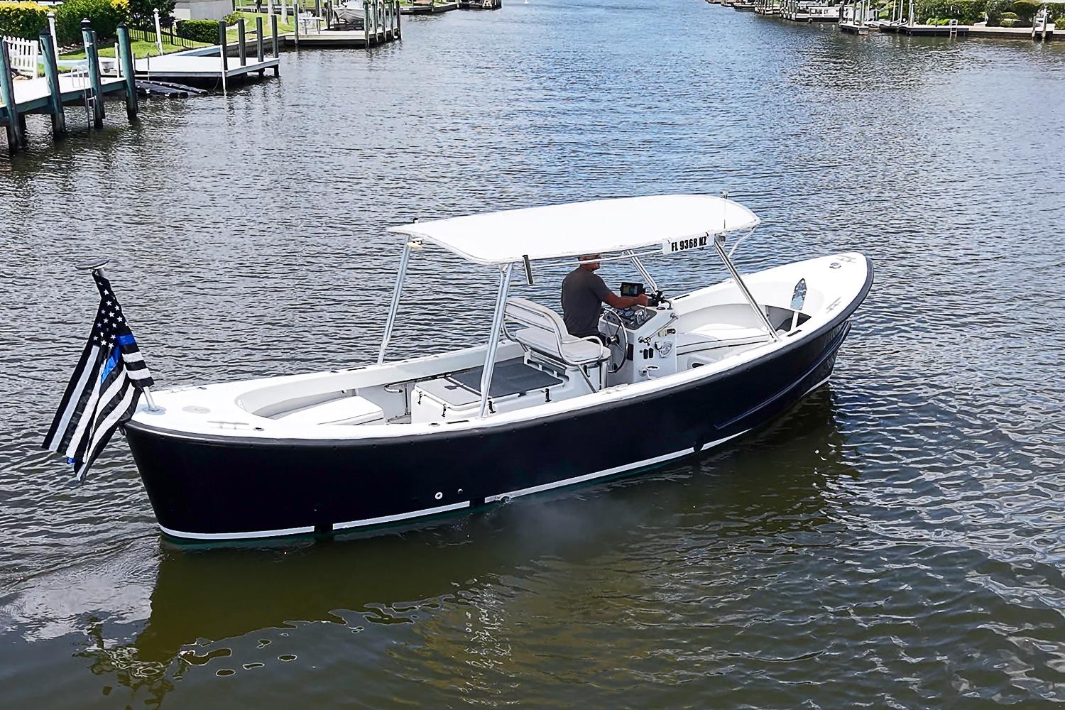 Custom 1969 boat with canopy and flag, cruising on a calm waterway.