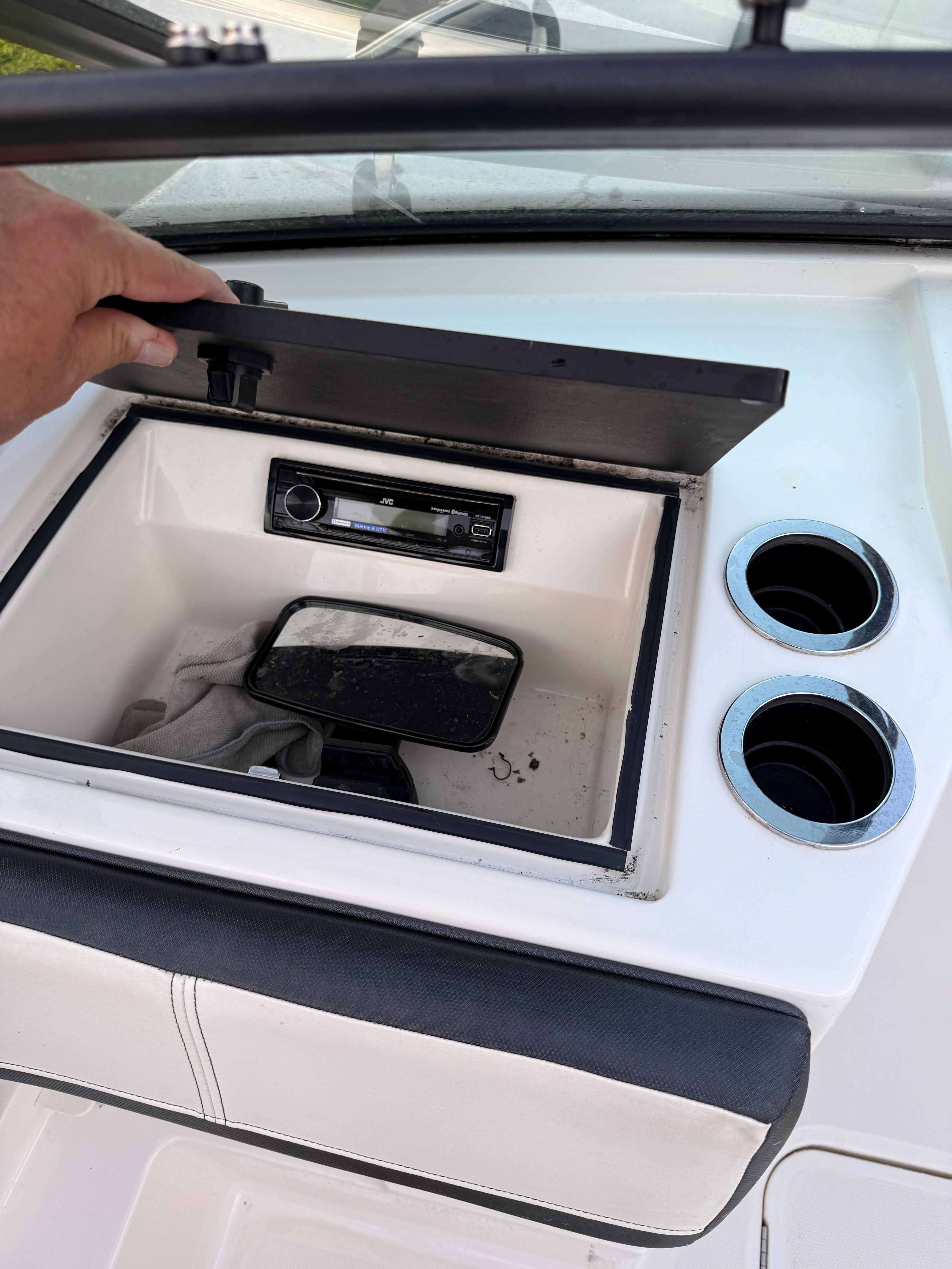 An open storage compartment on a Sea Ray SPX 210 Outboard boat with a radio and two cup holders.