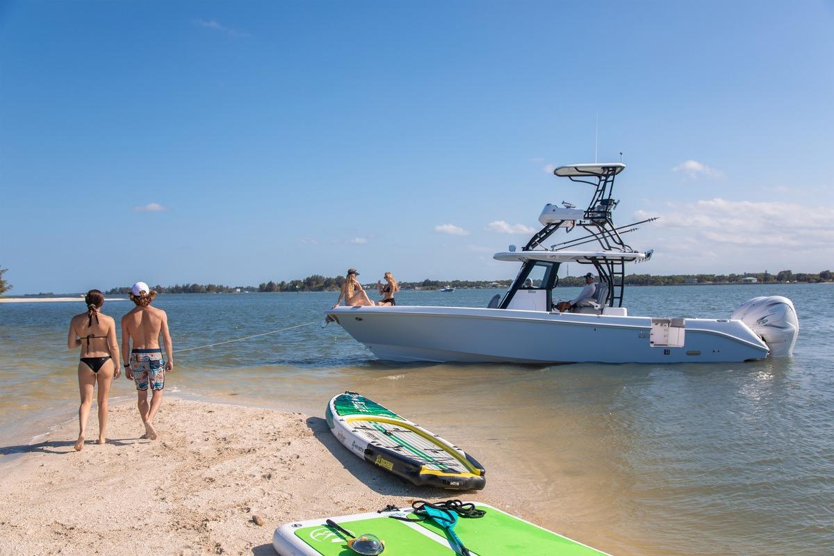 2026 Everglades 335 Center Console boat near sandy beach with paddleboards and people.