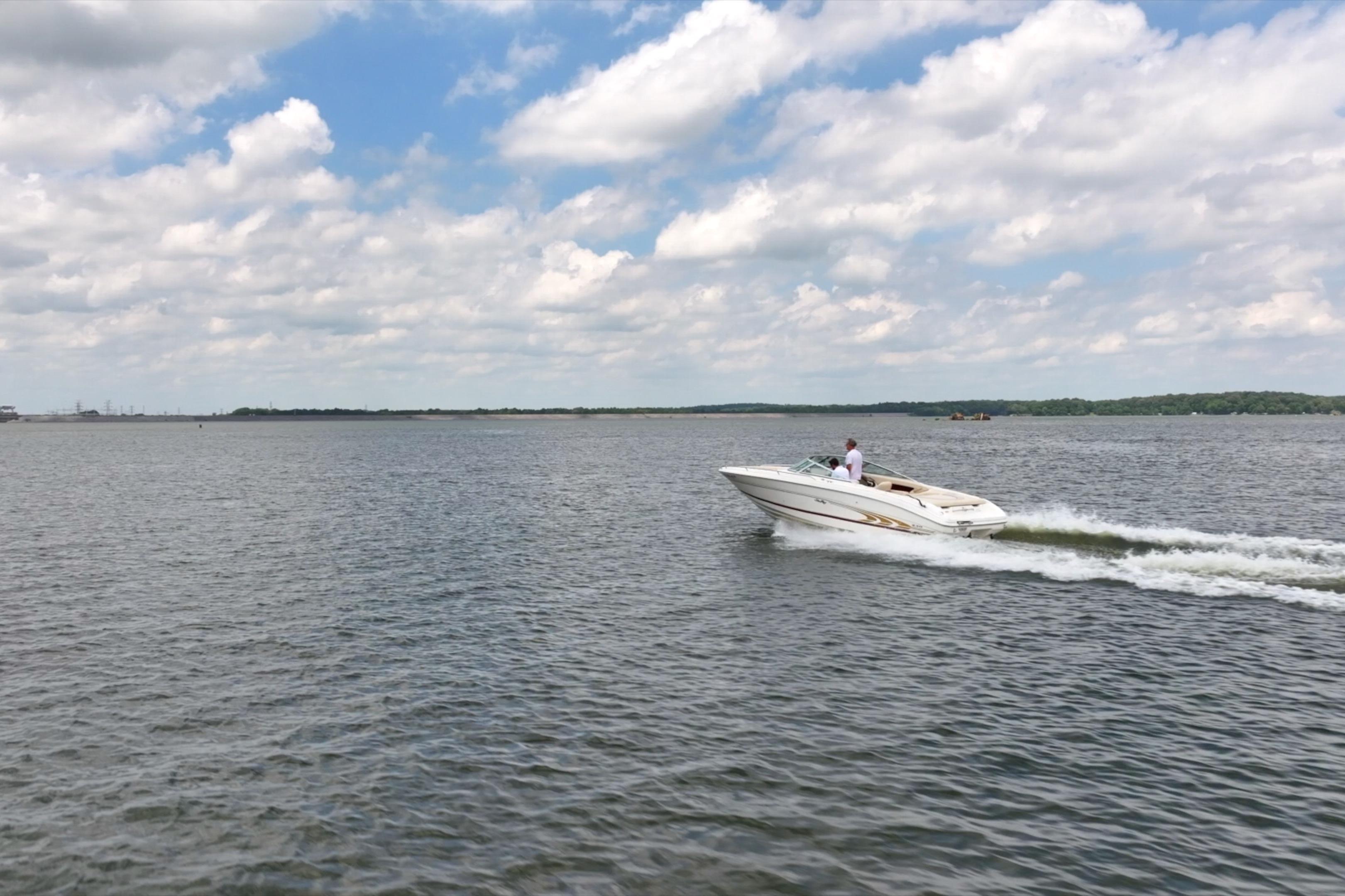 A 1997 Sea Ray 230 Signature boat cruising on a lake under a partly cloudy sky.
