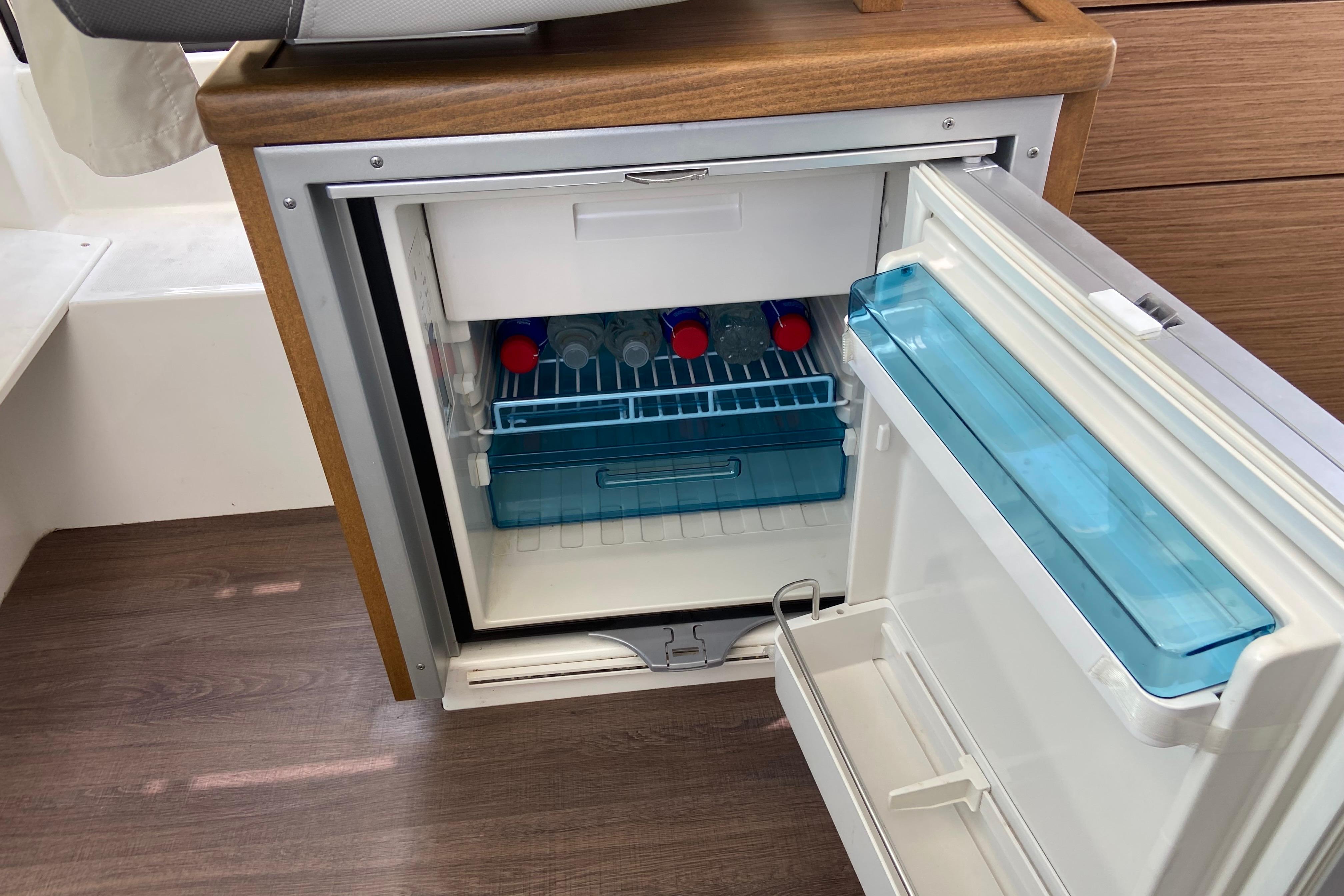 Compact fridge inside 2024 Jeanneau NC Weekender 895 Series 2 boat, stocked with bottles.