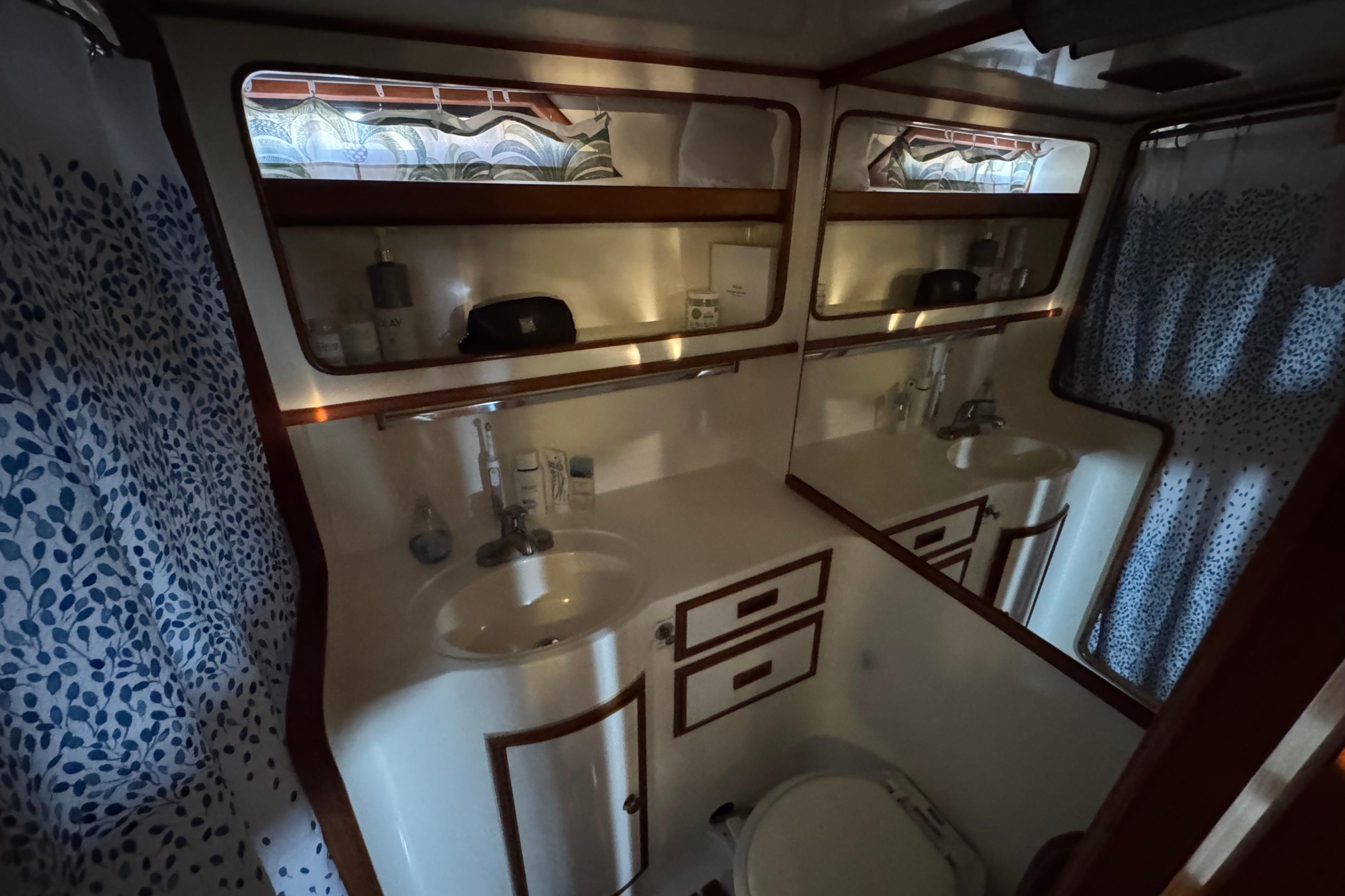 1987 President 37 yacht bathroom with sink, mirror, and patterned shower curtain.