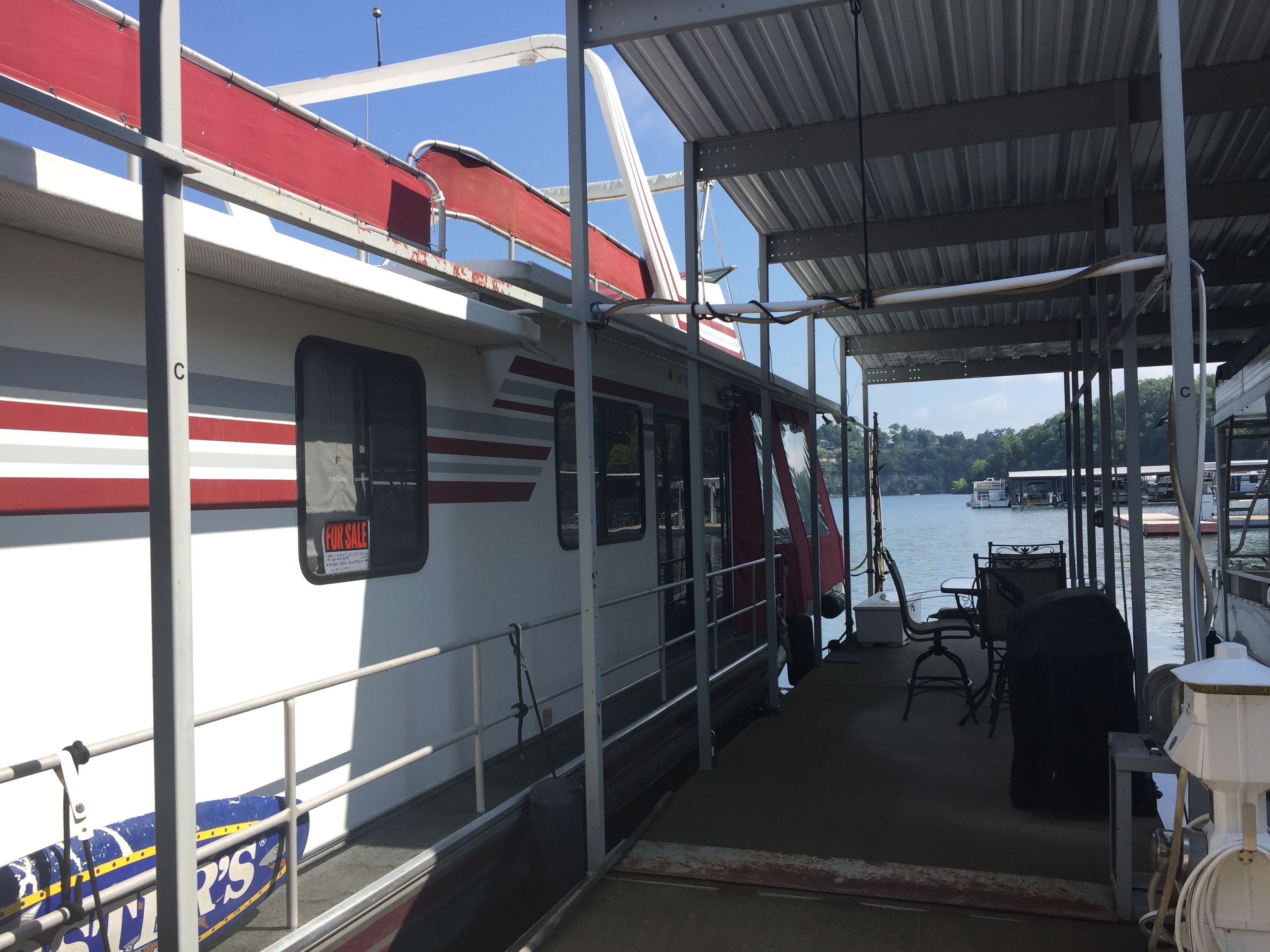 A 1989 Sumerset houseboat docked under a covered area, featuring red and white stripes.