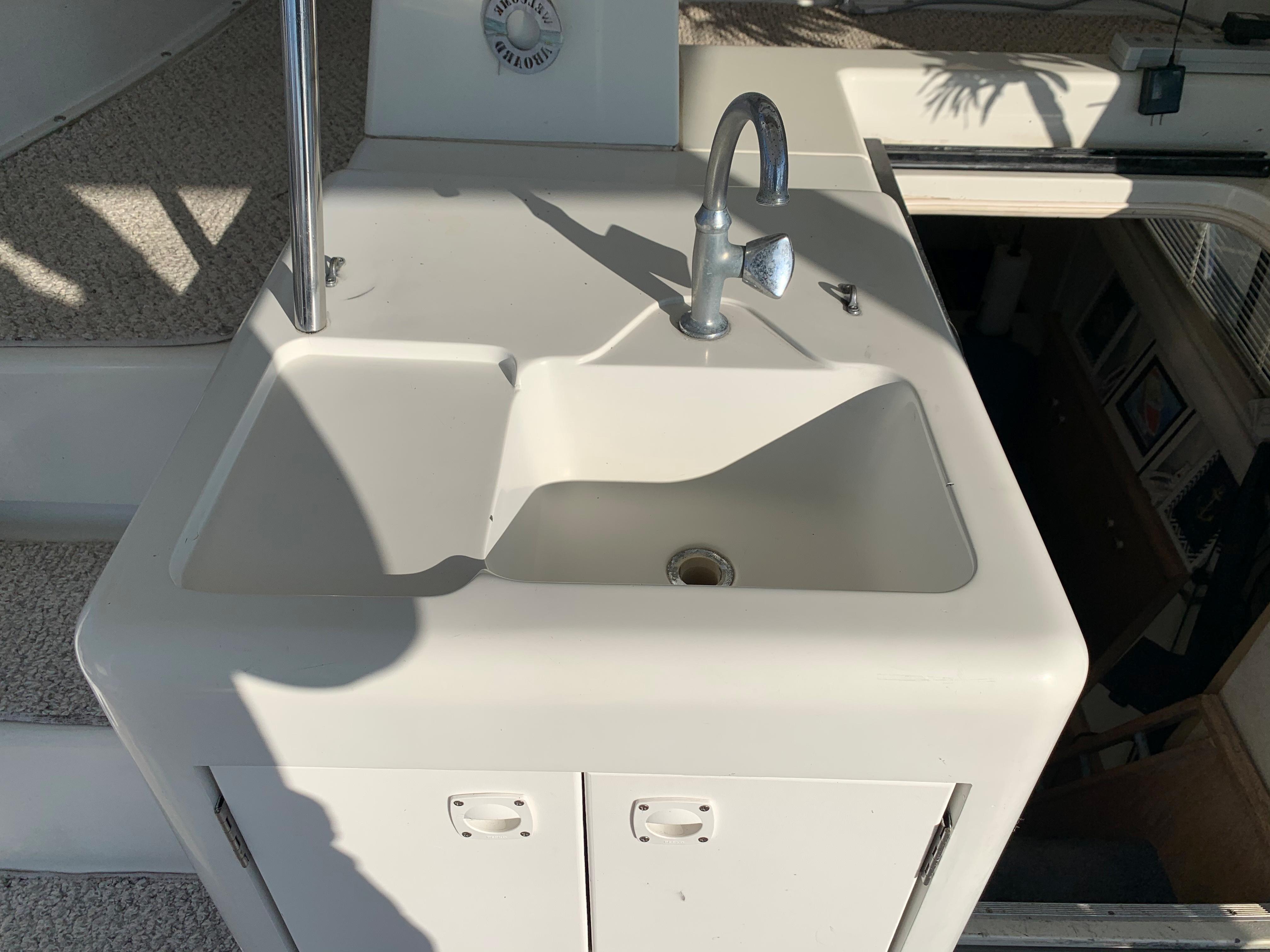 1992 Silverton 34 Aft Cabin Motor Yacht sink with faucet, white cabinetry, and sunlight.