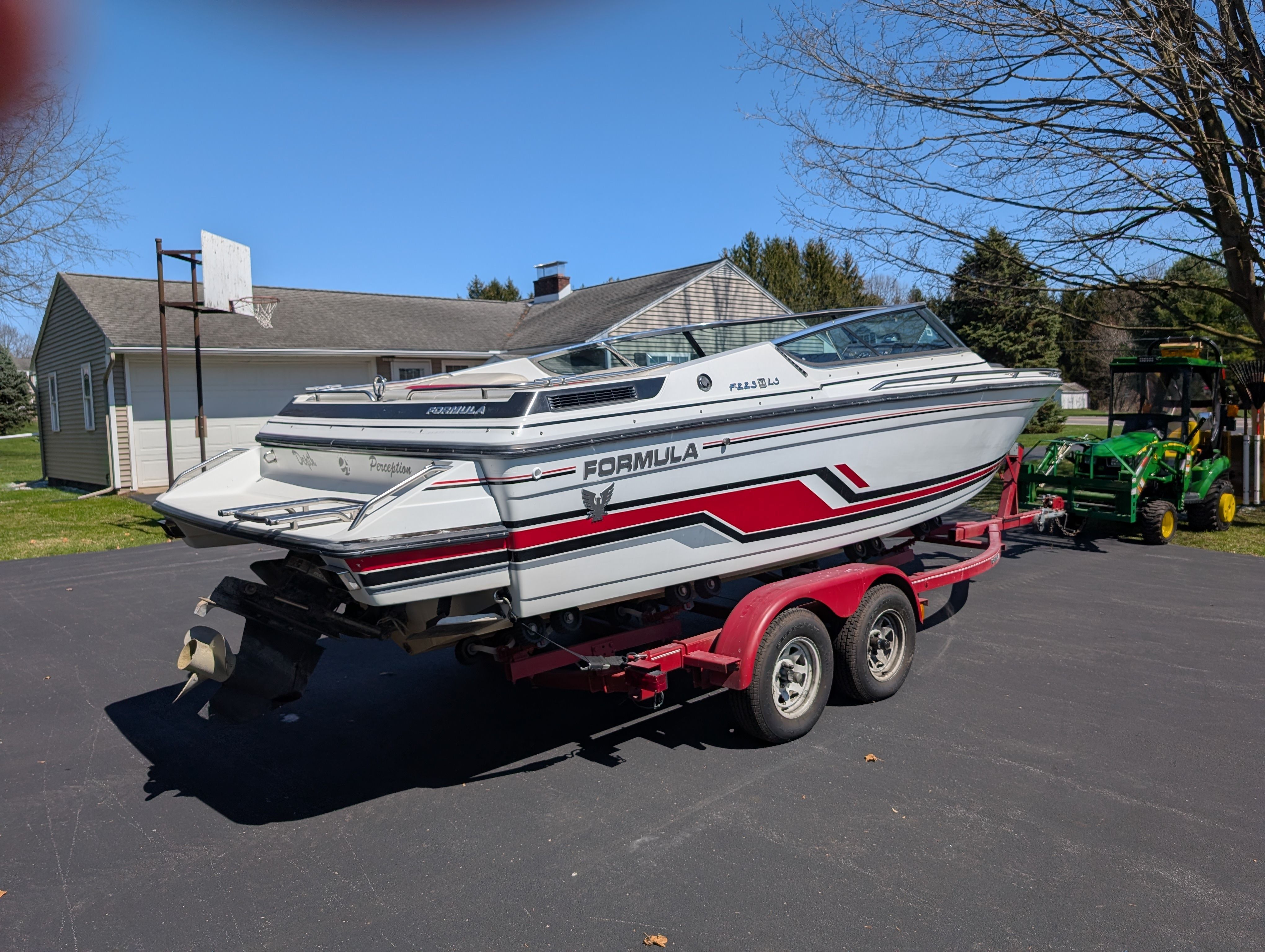 A white boat with red stripes sits on a trailer in a driveway.