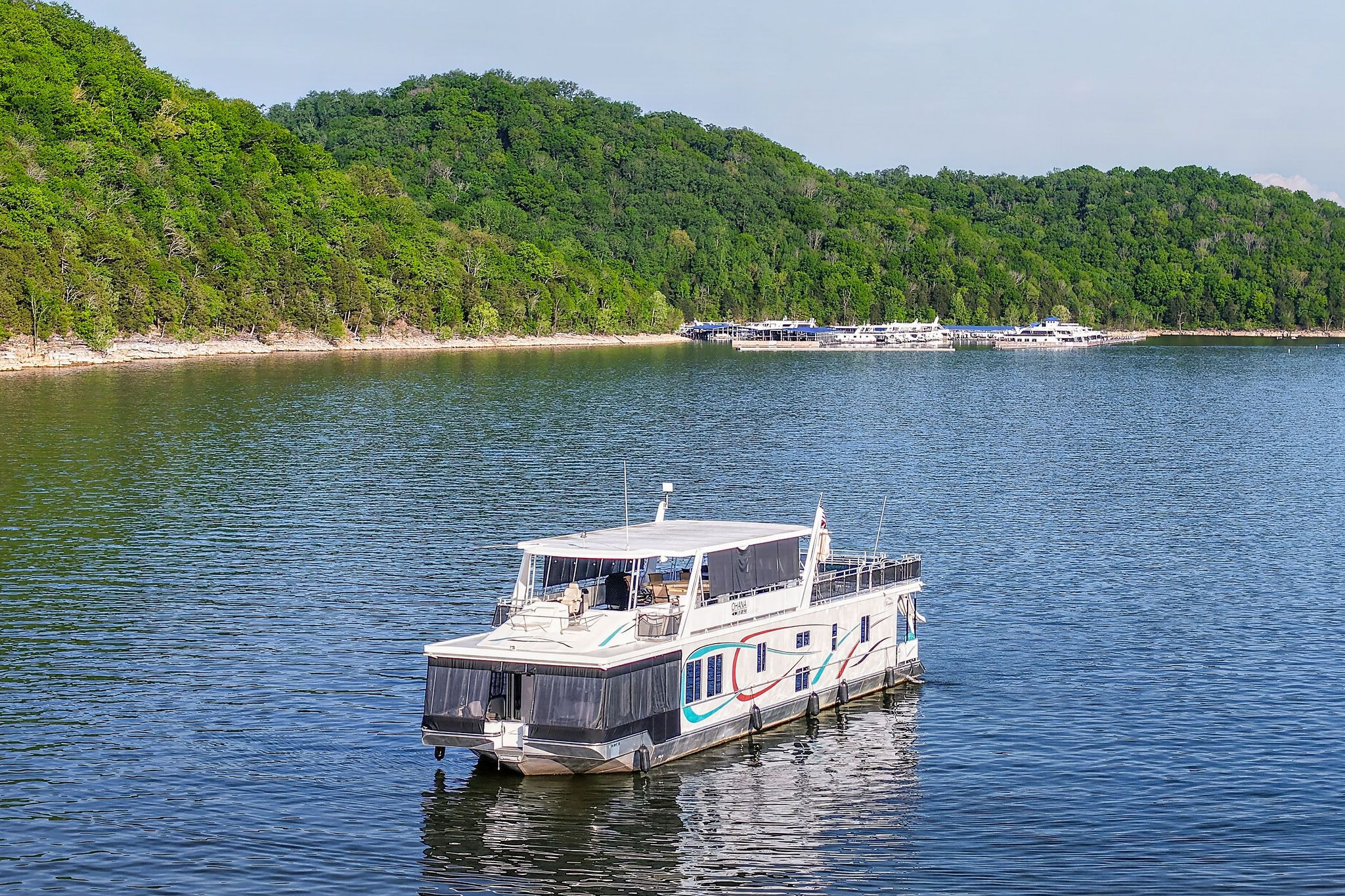 Houseboat on serene lake with wooded shores, model Throughbred 2010.