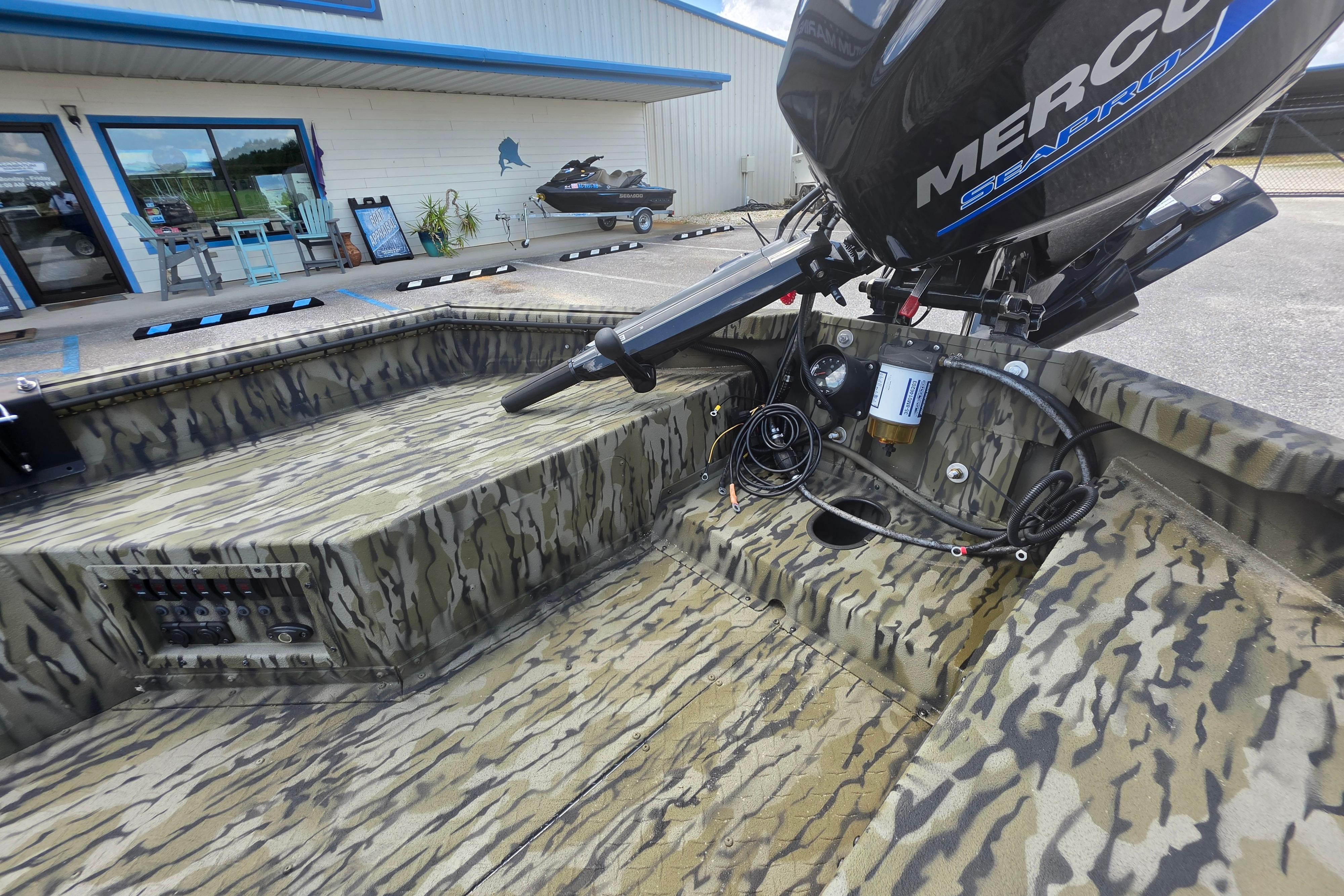 2025 SeaArk 1752 Slayer boat with camouflage design and Mercury engine, parked outside a building.