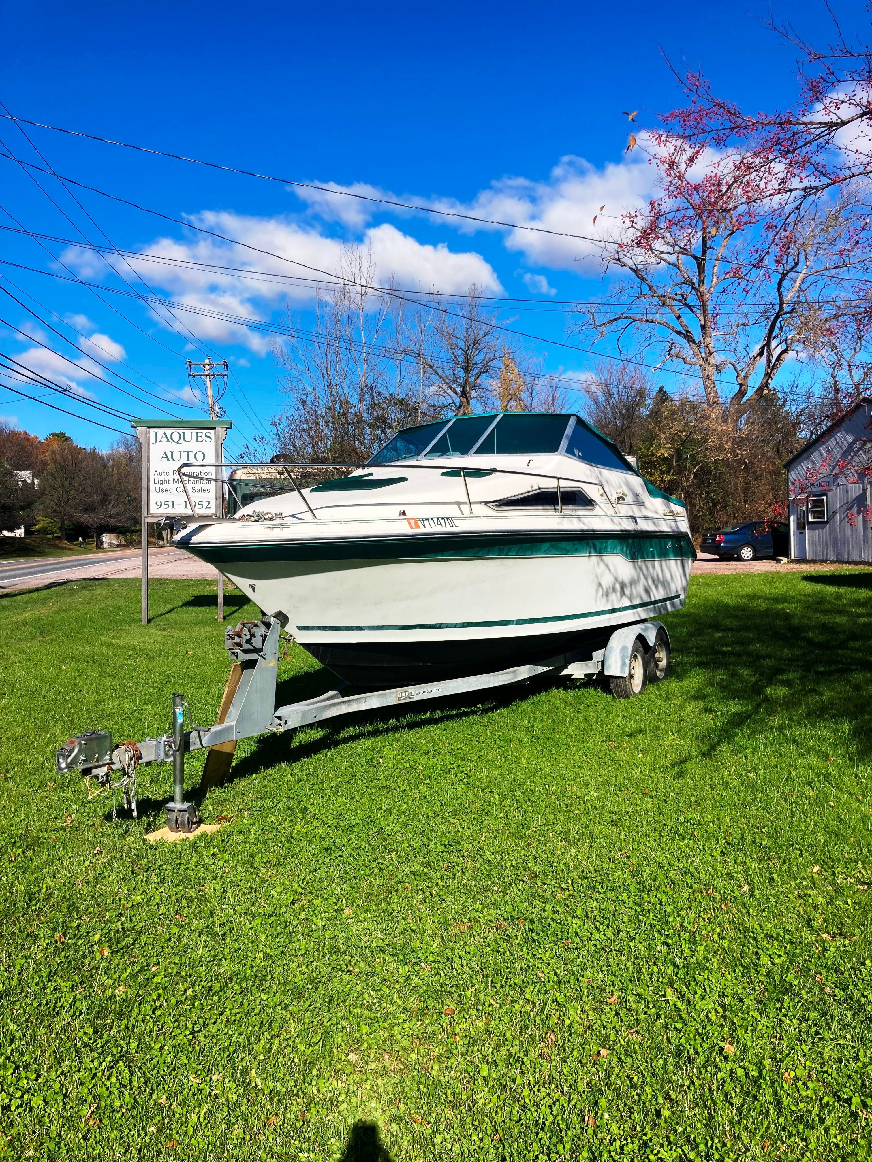 A 1991 Sea Ray 220 Sundancer on a trailer, parked on a grassy lawn.
