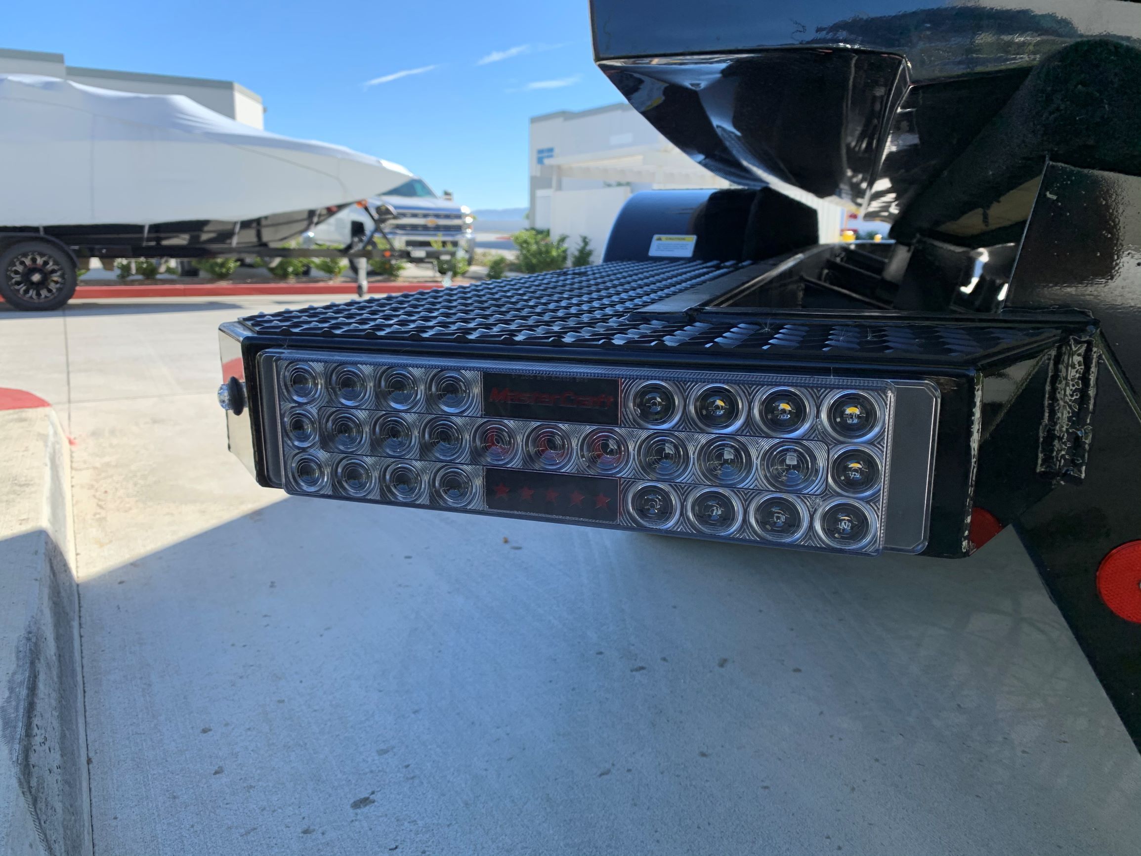 Close-up of a boat trailer with LED lights, another boat in the background.
