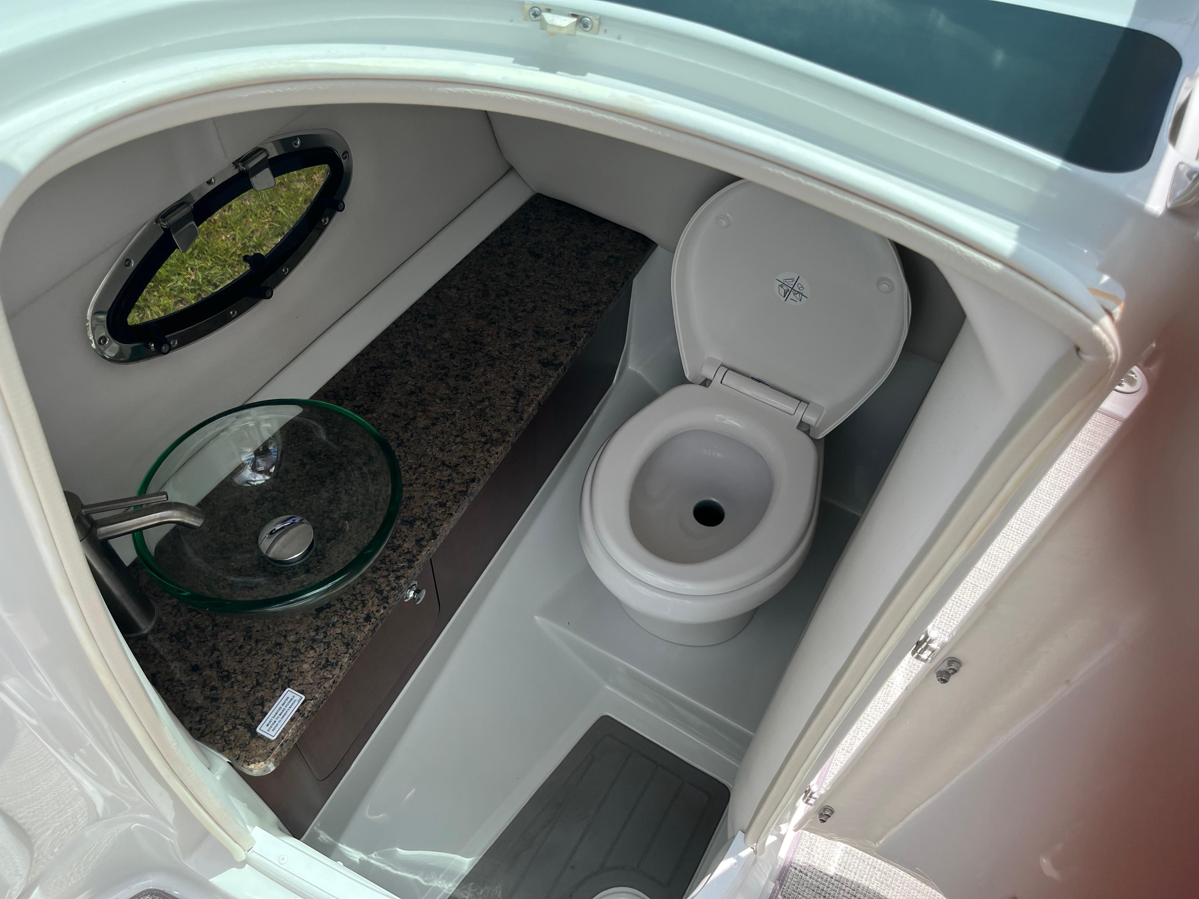 The image shows a boat toilet with a round sink and a porthole.