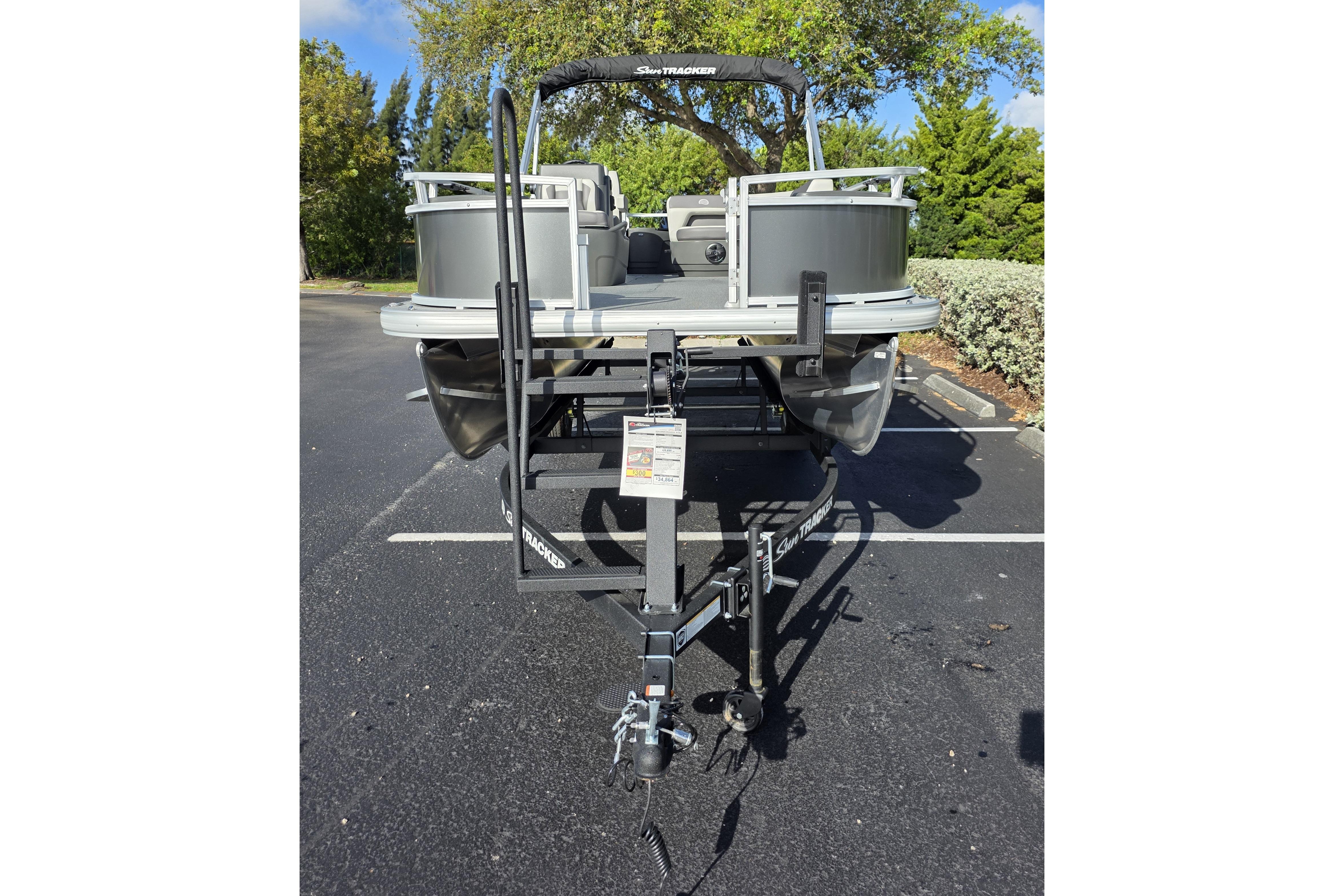 2026 Sun Tracker Bass Buggy 16 XL Select pontoon boat on trailer in parking lot.