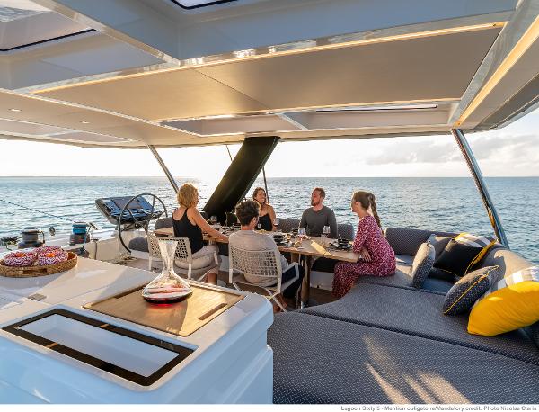 Luxurious Lagoon SIXTY 5 yacht deck with people dining, ocean view, 2025 model.