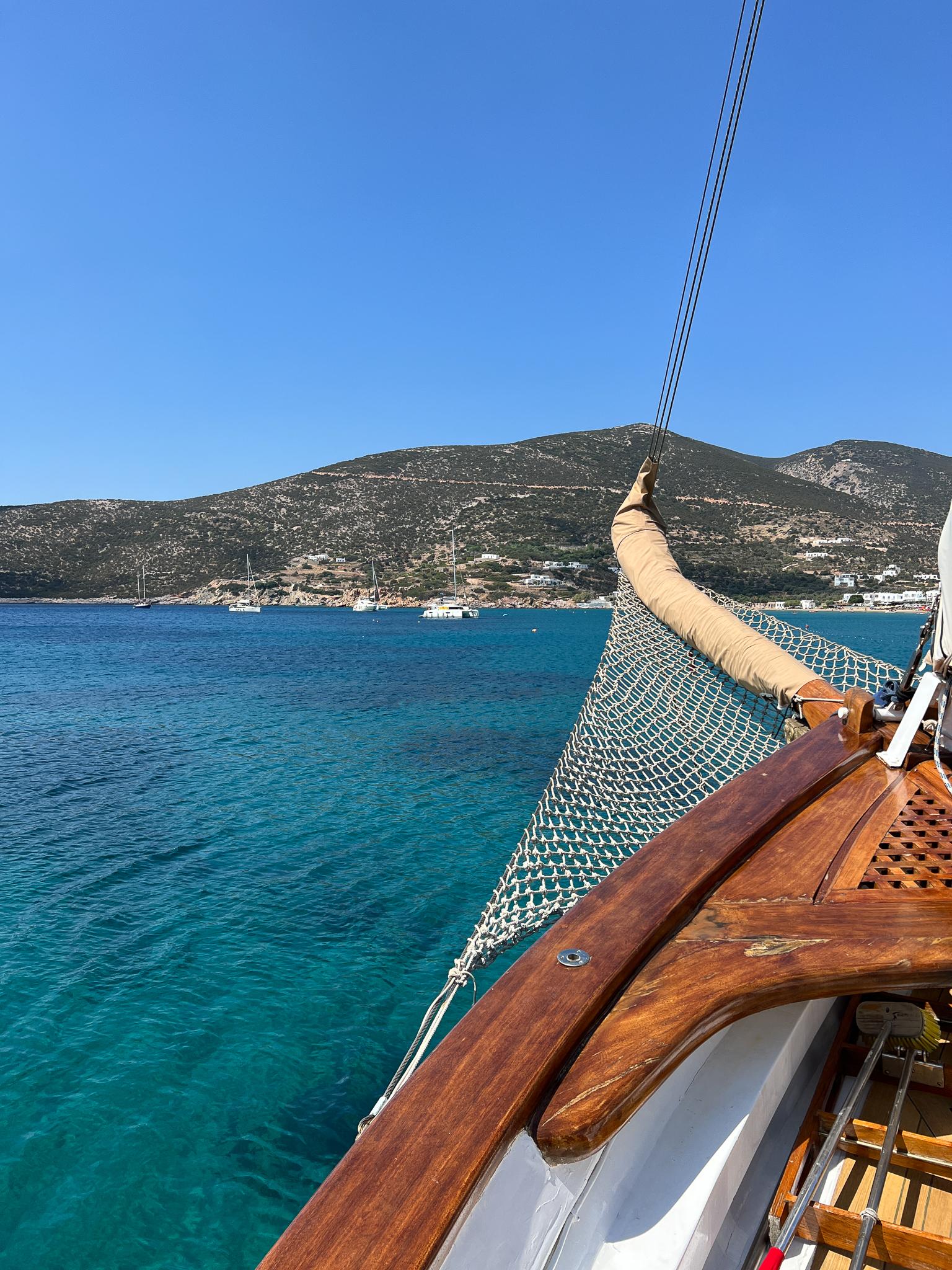 Sailing yacht by Psarros Shipyard (1969) on clear blue sea with scenic mountain backdrop.