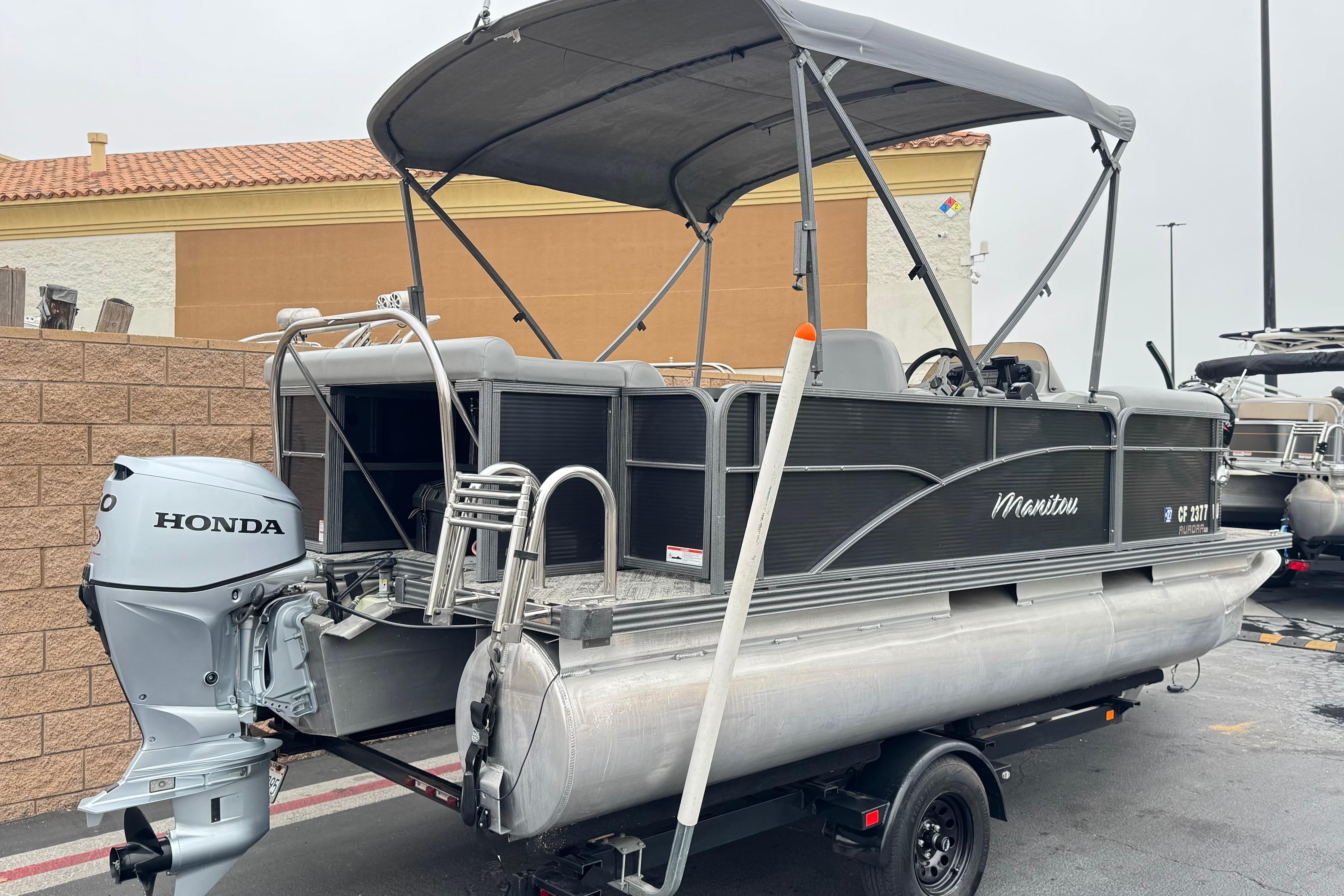 2020 Manitou 18 Aurora LE pontoon boat with Honda outboard motor, parked on trailer.