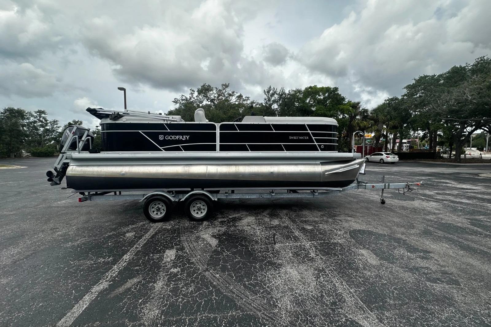 2023 Godfrey 2286 pontoon boat on trailer in parking lot, cloudy sky background.