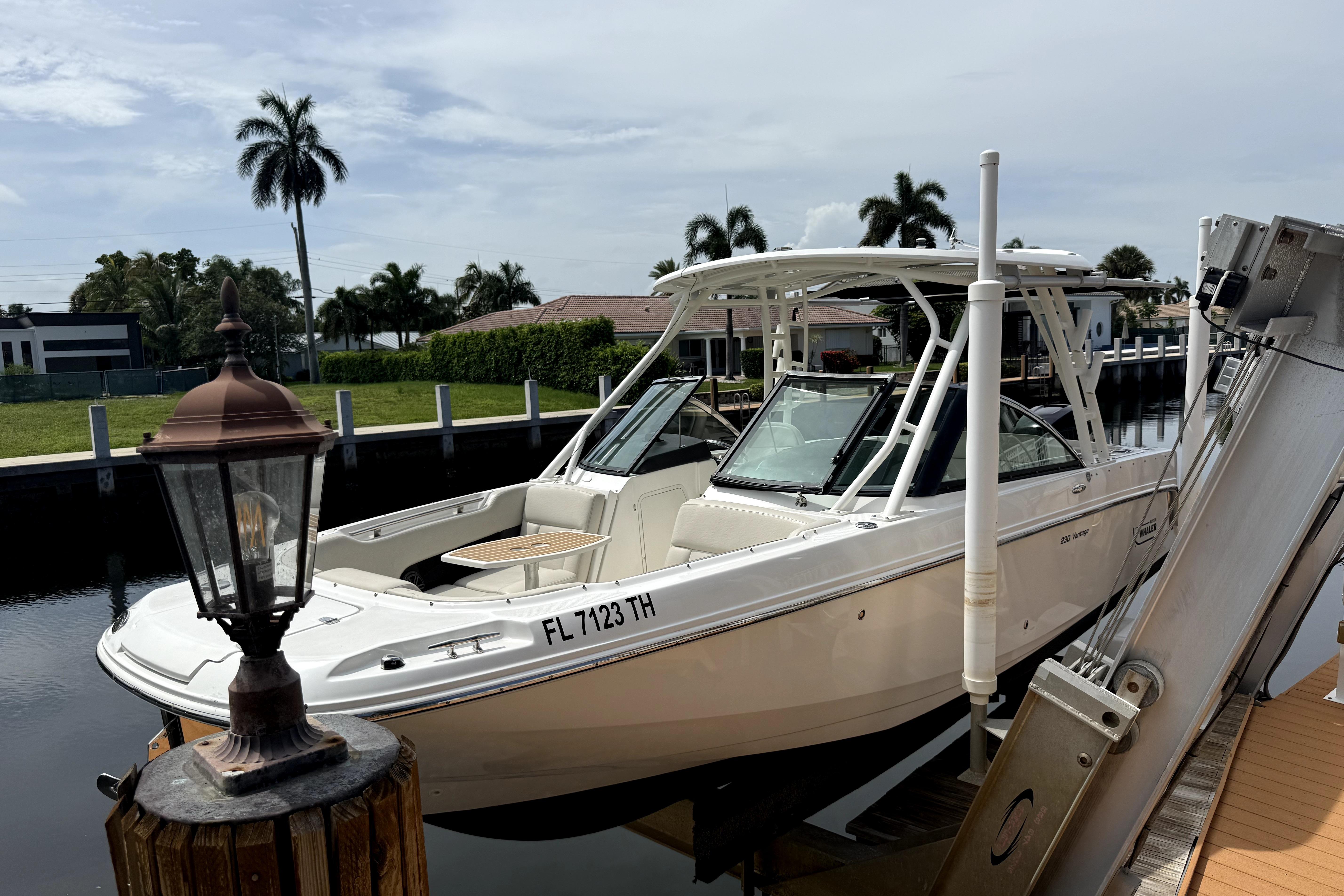 2018 Boston Whaler 230 Vantage boat docked near palm trees and waterfront homes.