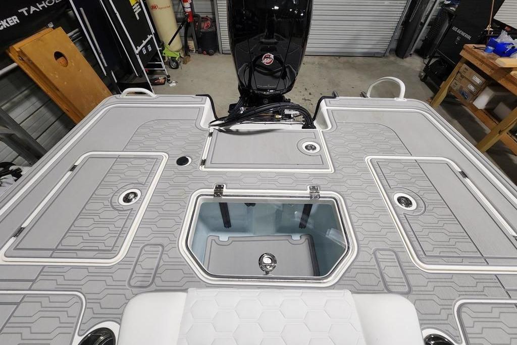 2026 Mako 18 Pro Skiff boat deck with storage compartments and motor in a garage.
