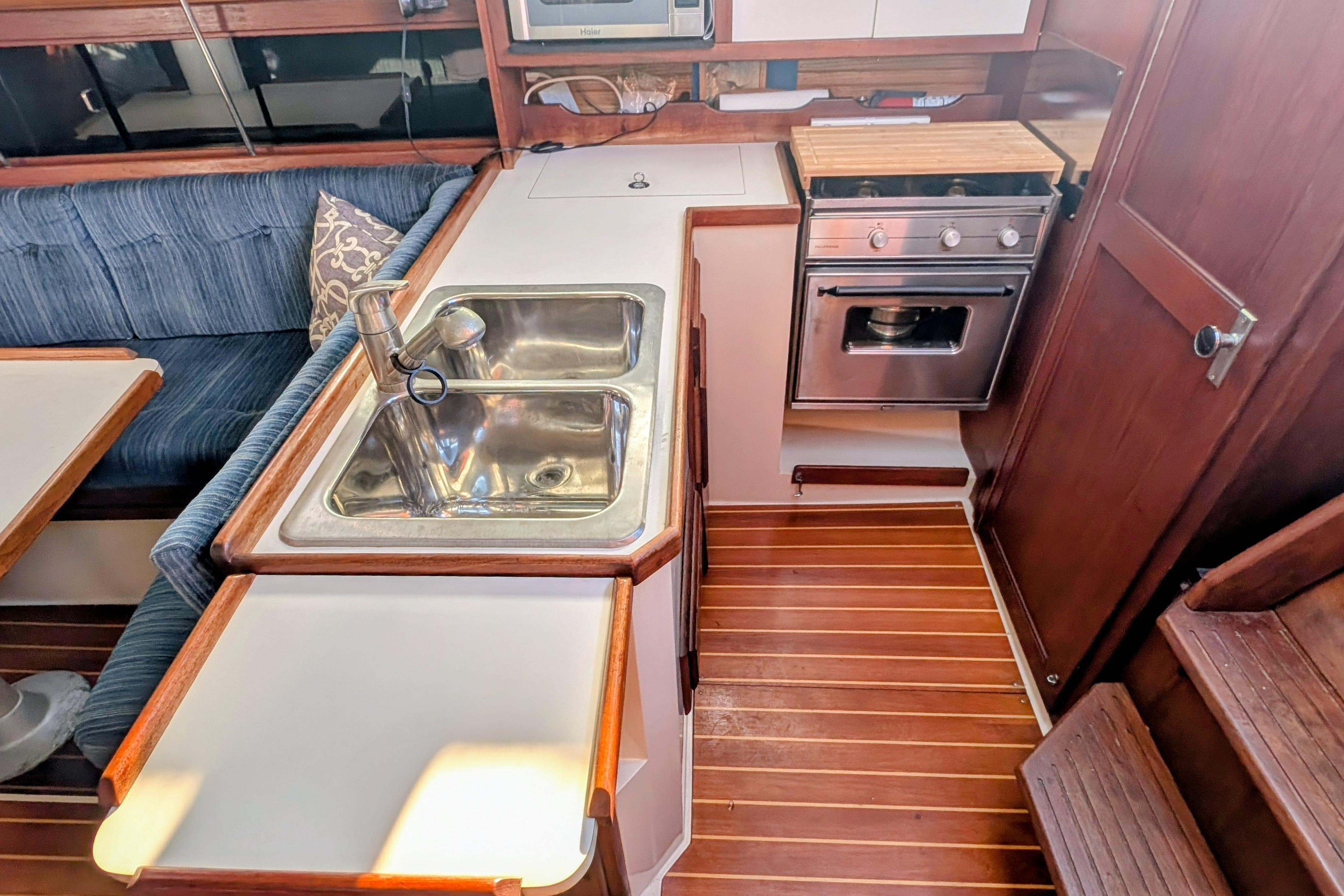Interior of 1989 Catalina 34 sailboat kitchen with sink, stove, and wooden flooring.
