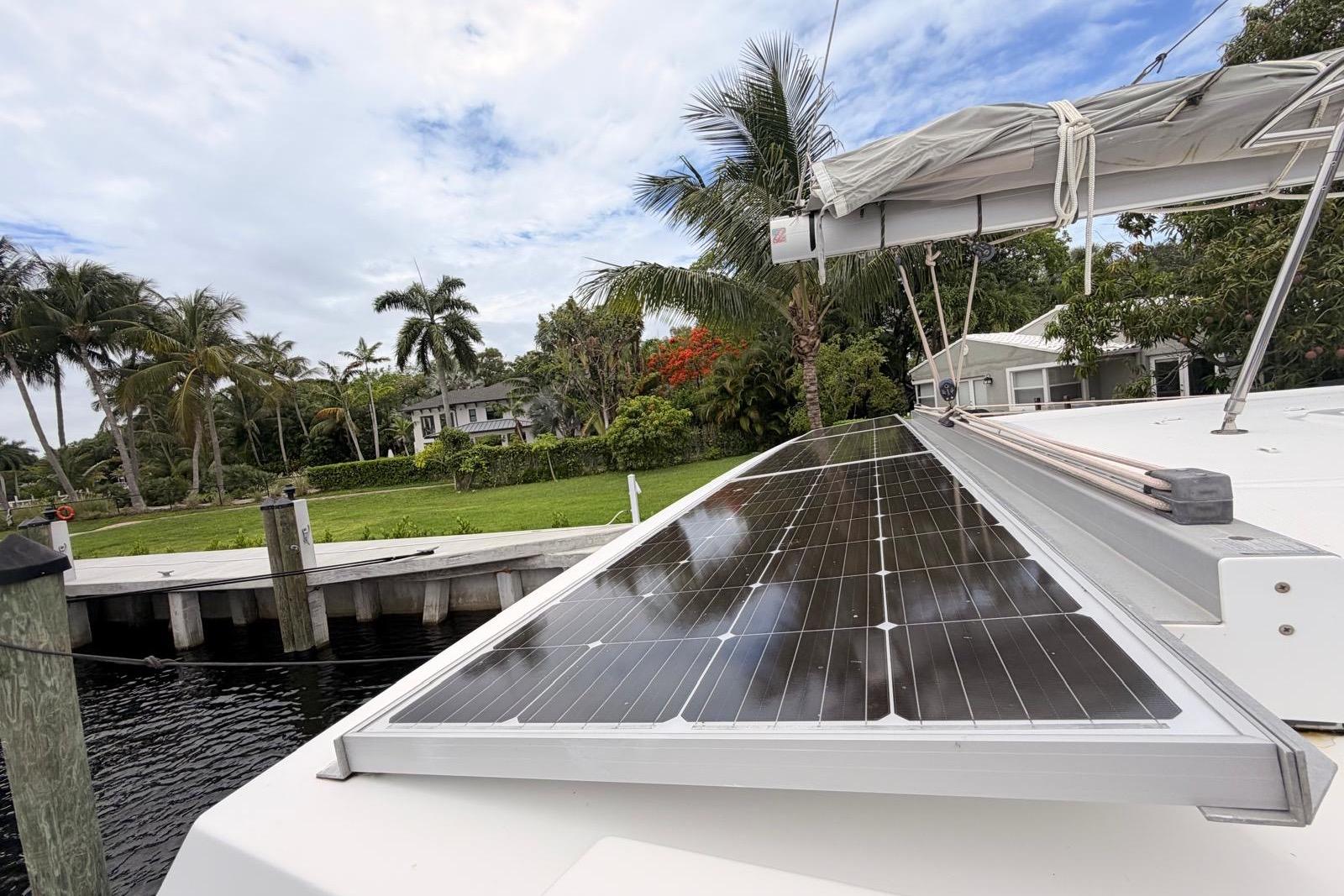 2018 Fountaine Pajot Lucia 40 catamaran with solar panels, docked near lush greenery and palm trees.