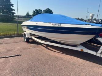 2005 Bayliner 205 Bowrider boat on trailer with blue cover, parked outdoors.
