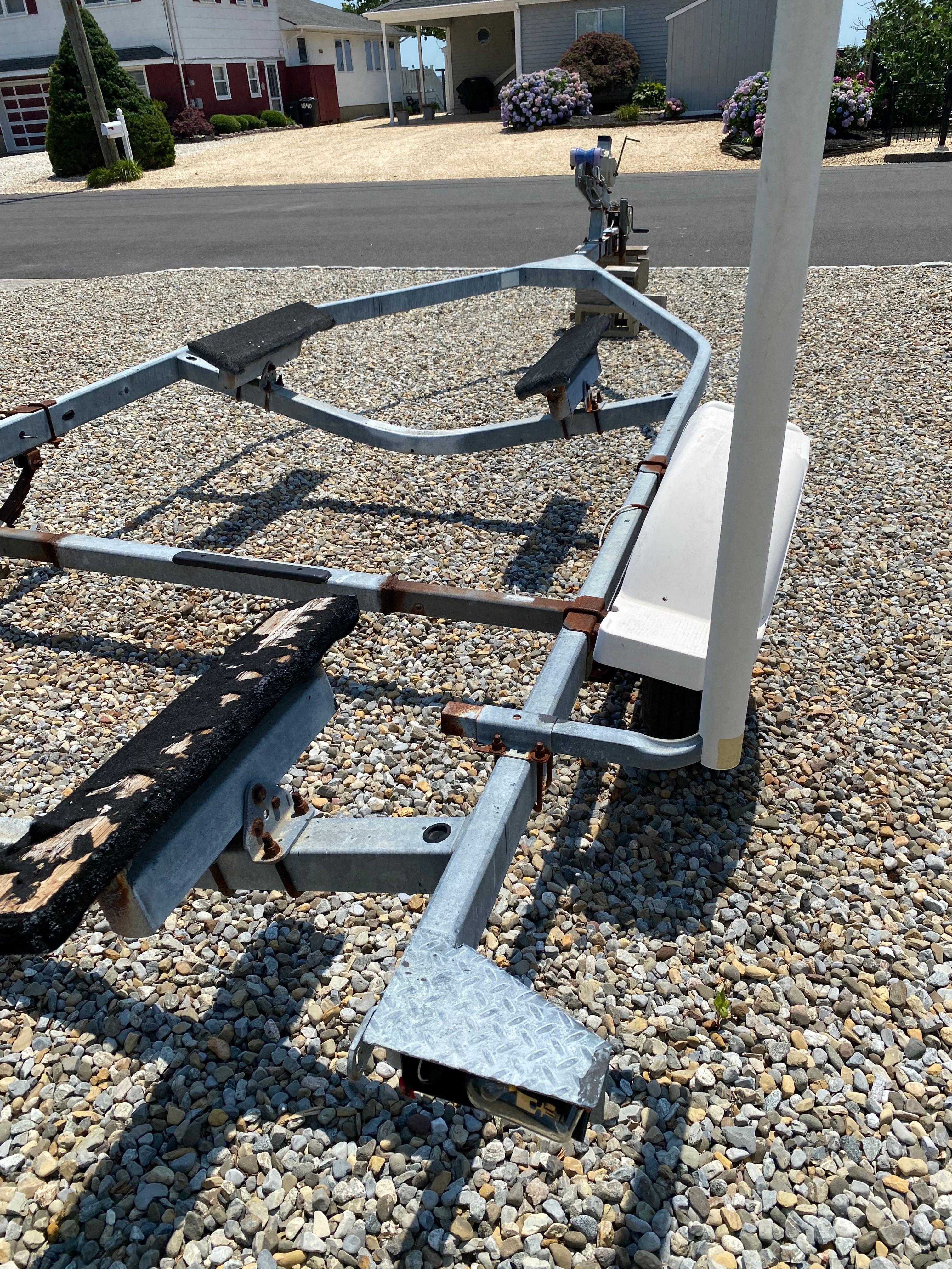 A boat trailer sits on a gravel driveway in a residential area.