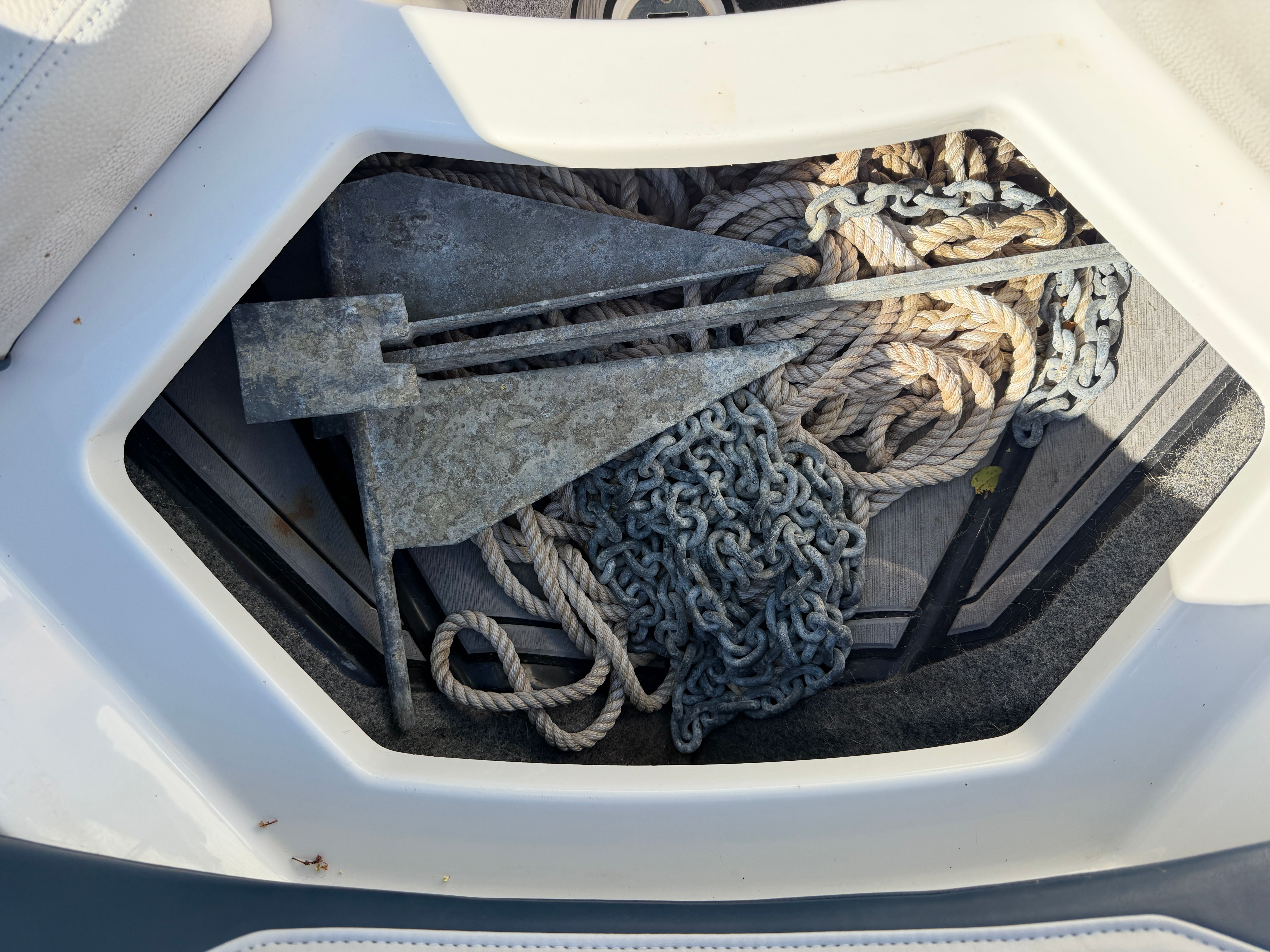 An anchor and ropes are stored in a compartment on a boat.