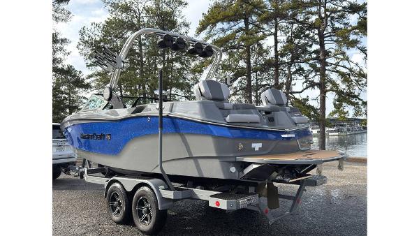 2023 MasterCraft XT22 boat on trailer, parked near trees and water.