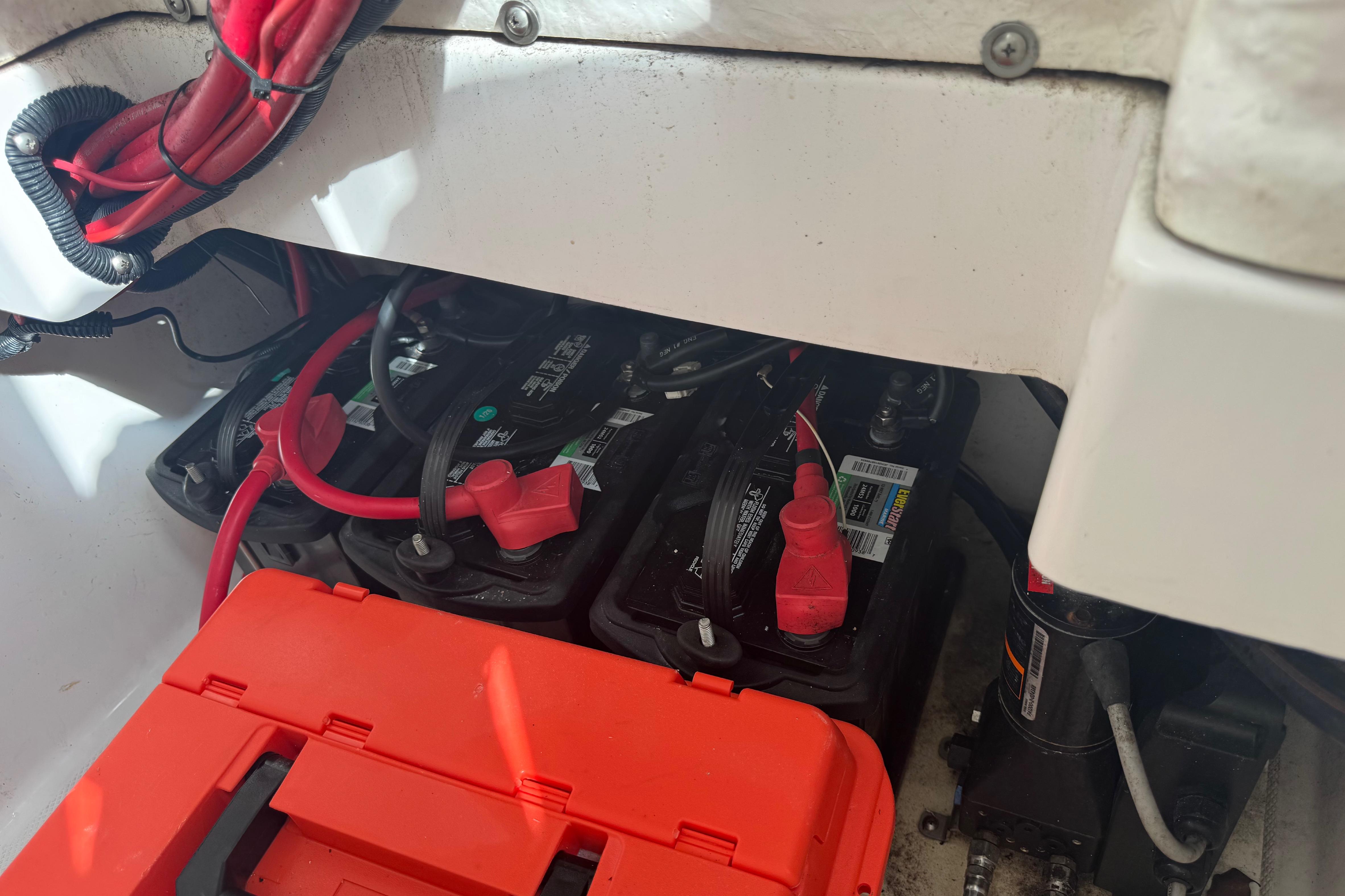 Battery compartment of 2022 Aquasport 2500 Center Console with red cables and orange cover.