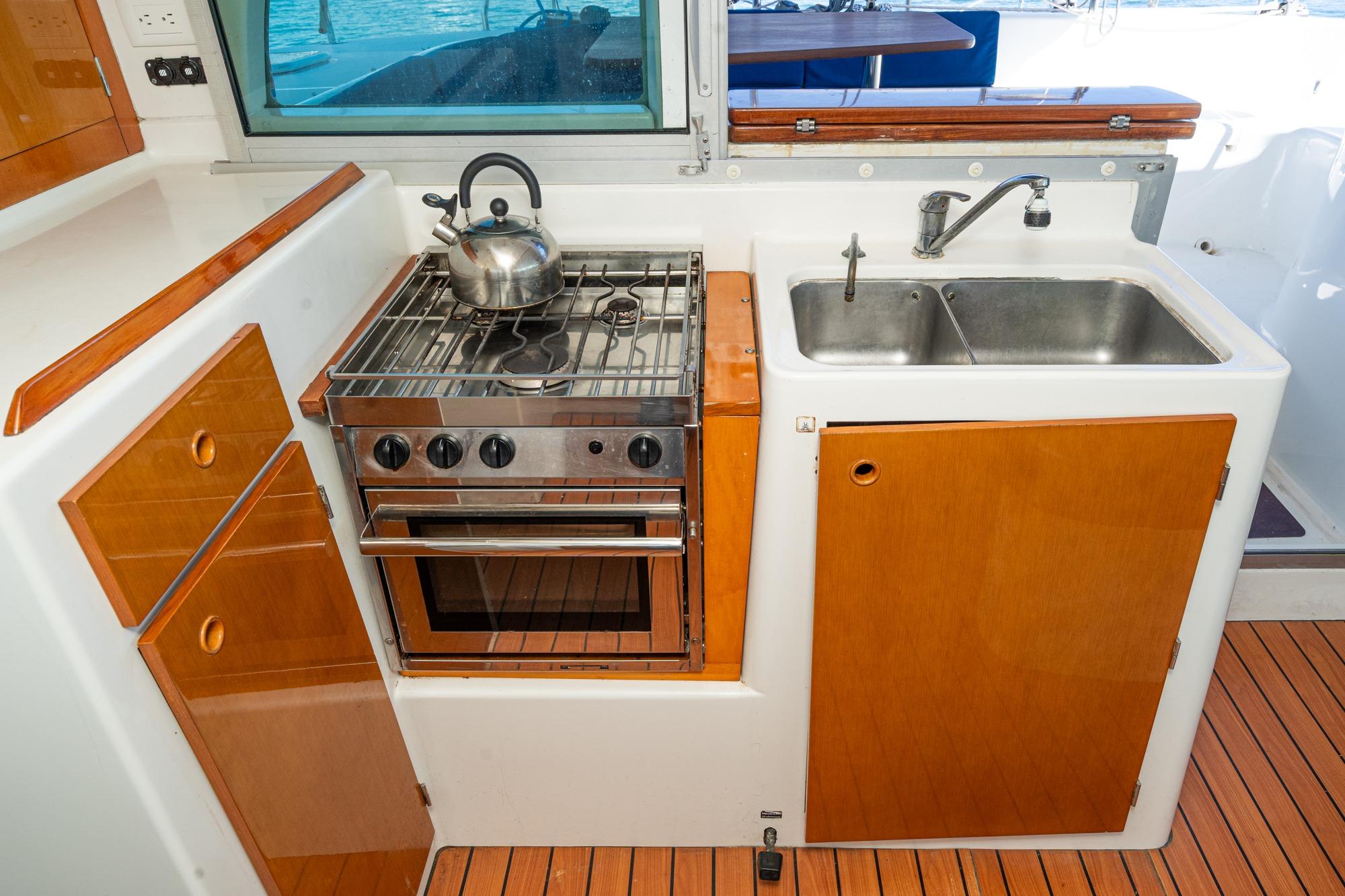 Compact kitchen in a 2004 Lagoon 380 yacht with stove, sink, and wooden cabinetry.