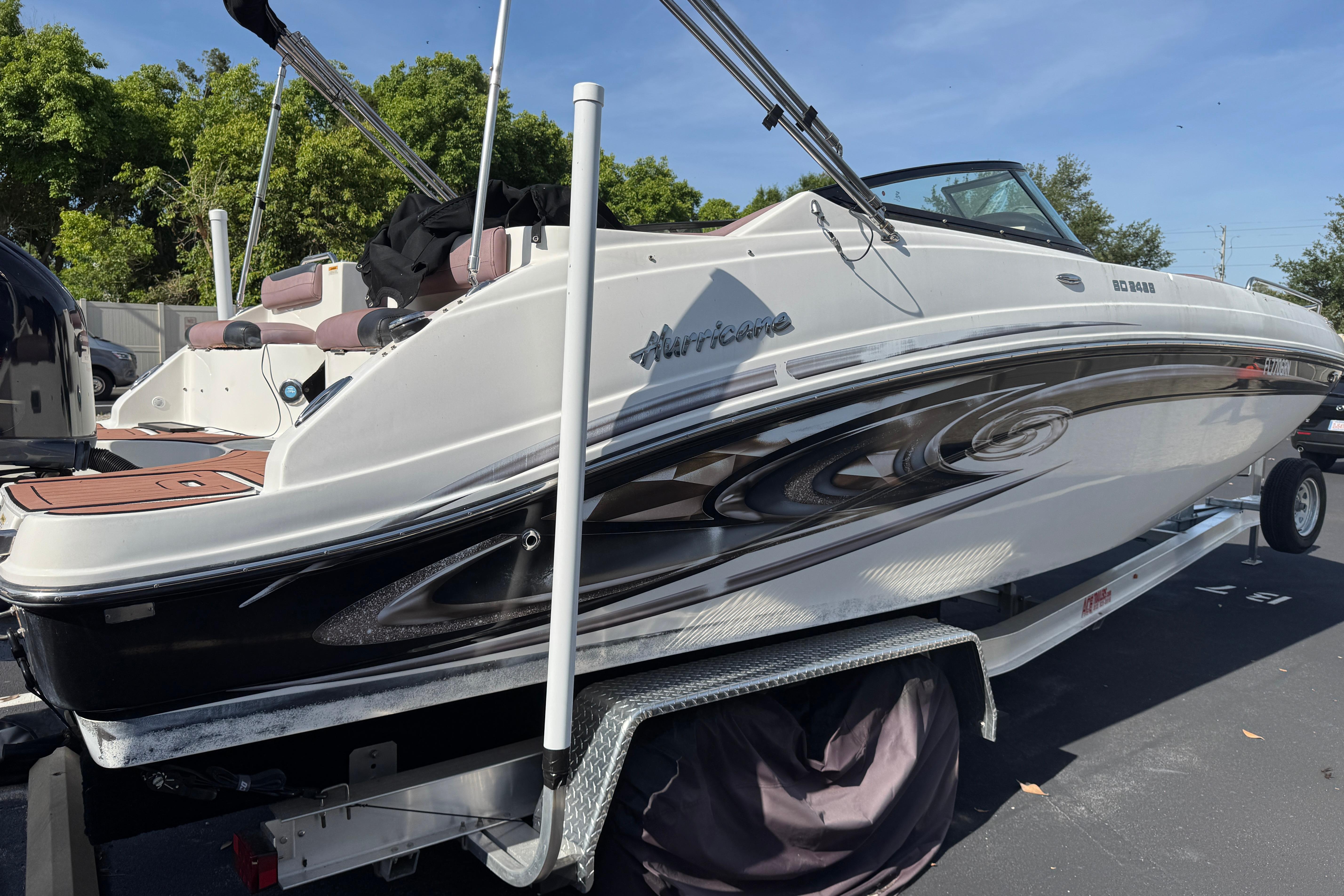 2018 Hurricane SunDeck 2400 OB boat on trailer, parked outdoors with trees in background.