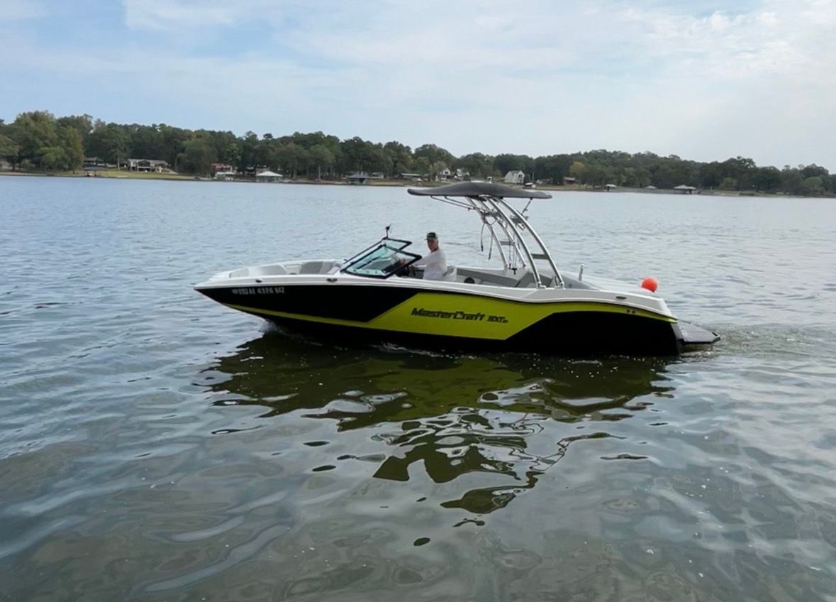 A 2017 MasterCraft NXT22 on a calm lake with a wooded shoreline.