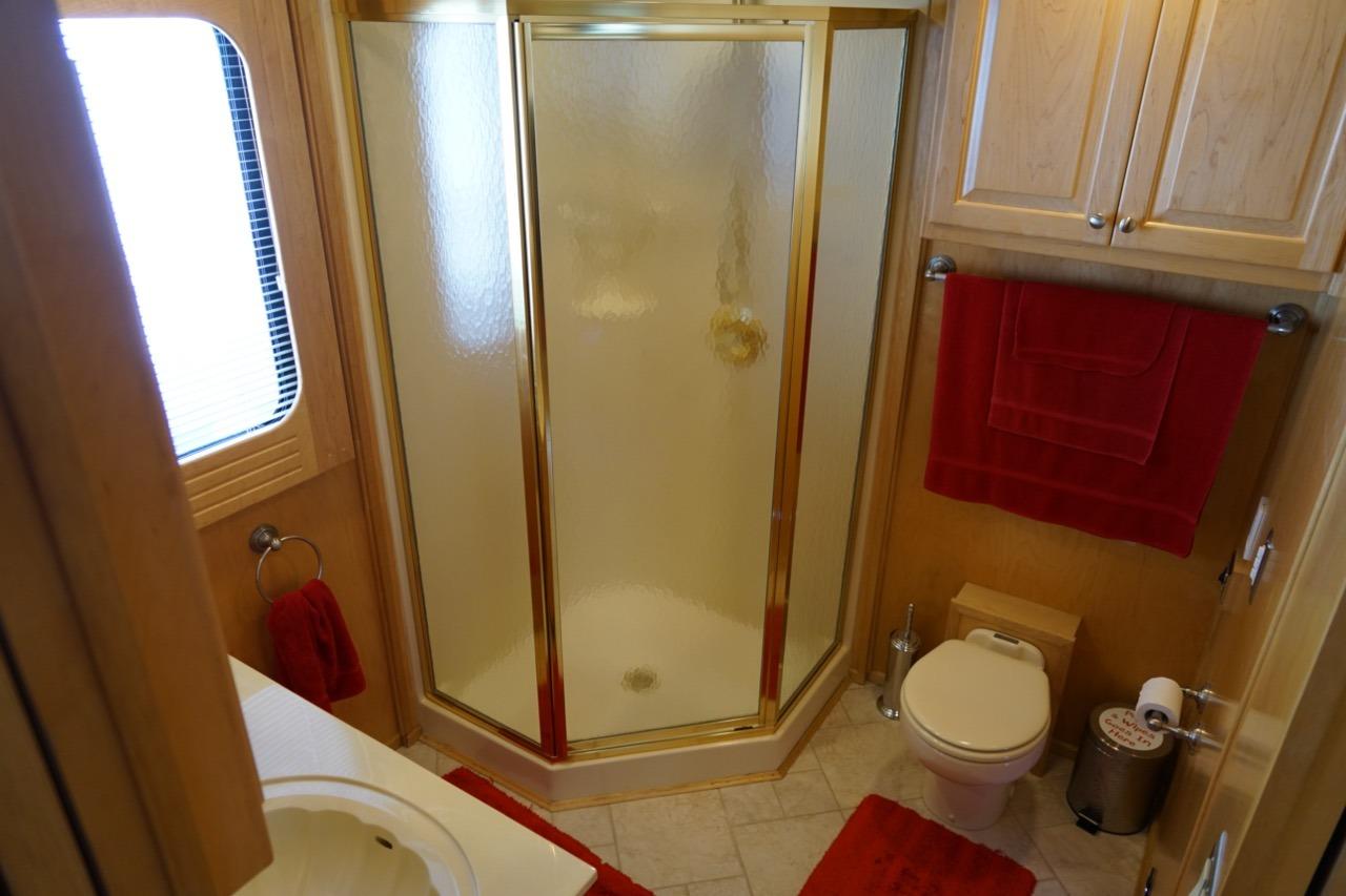 Luxurious bathroom in 2000 Stardust Cruisers houseboat with shower, red accents, and wooden cabinetry.