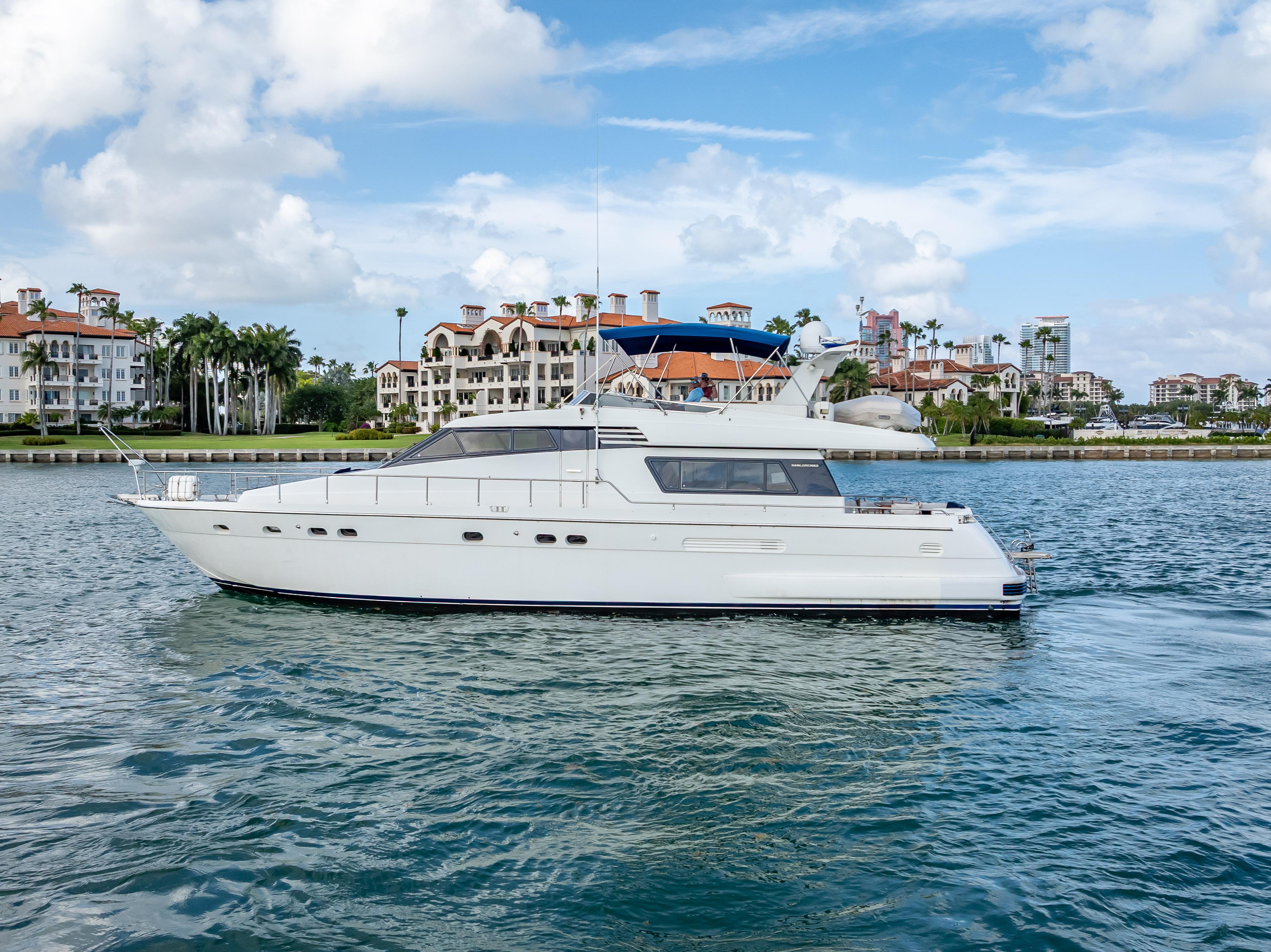 Sanlorenzo 62 yacht from 1995 cruising on a scenic waterfront with luxury homes.