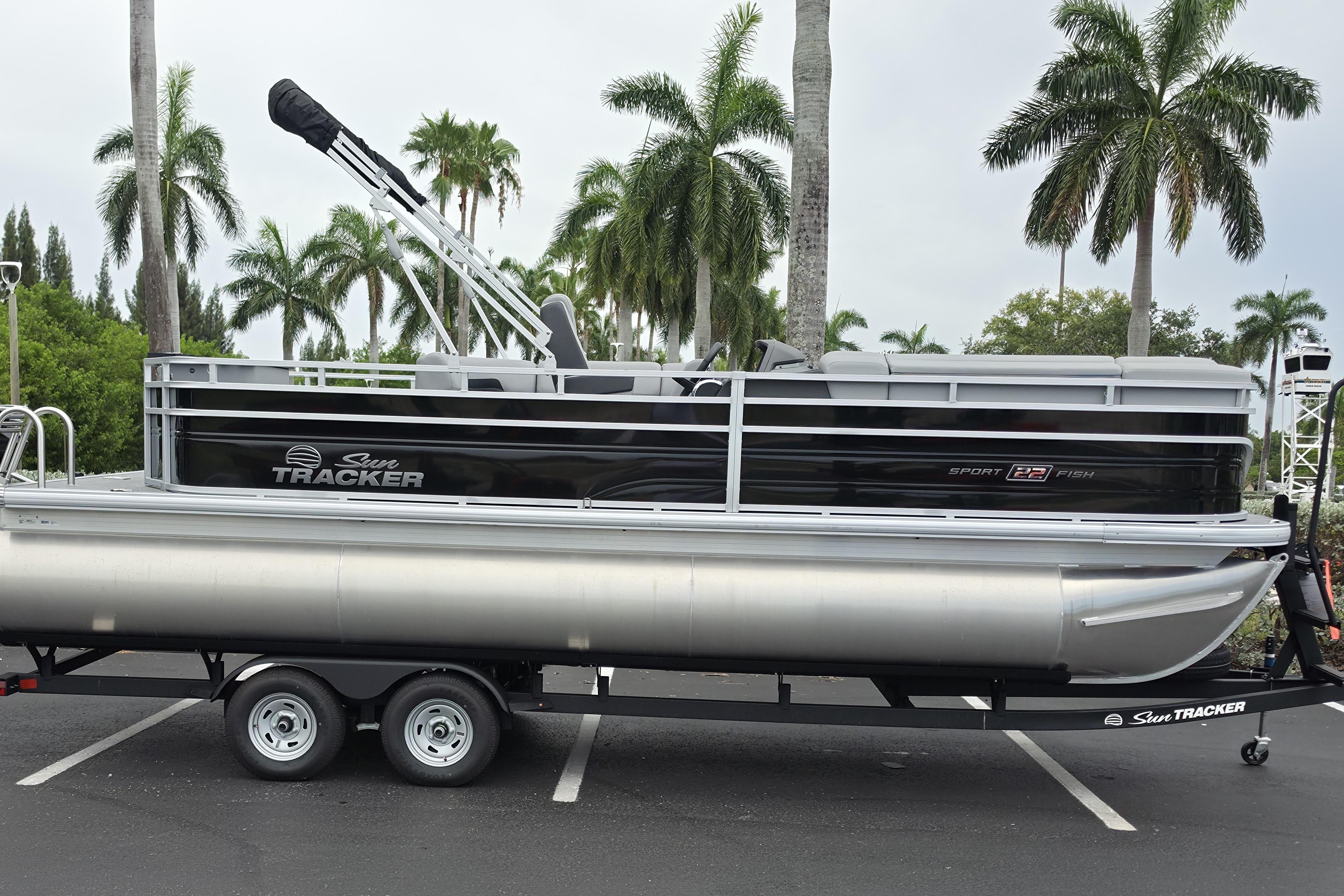 2026 Sun Tracker SportFish 22 XP3 pontoon boat on trailer, surrounded by palm trees.