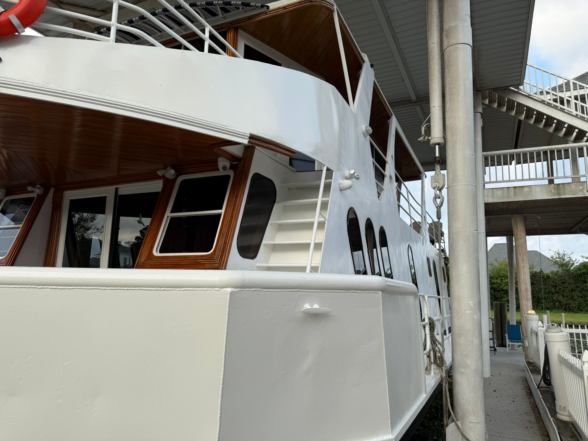 A white boat with wooden accents is docked. It features multiple windows and a staircase.
