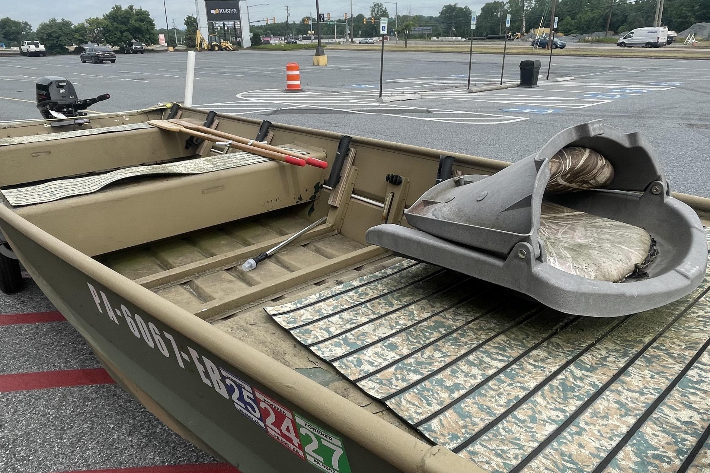 1986 Landau 1664 Jon boat in parking lot, featuring camouflage interior and outboard motor.