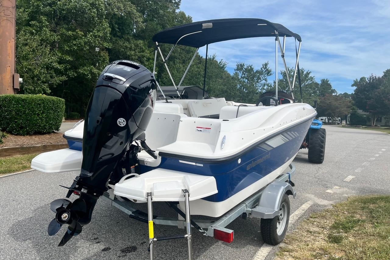 2026 Bayliner Element E16 boat on trailer, parked on a road with trees in background.