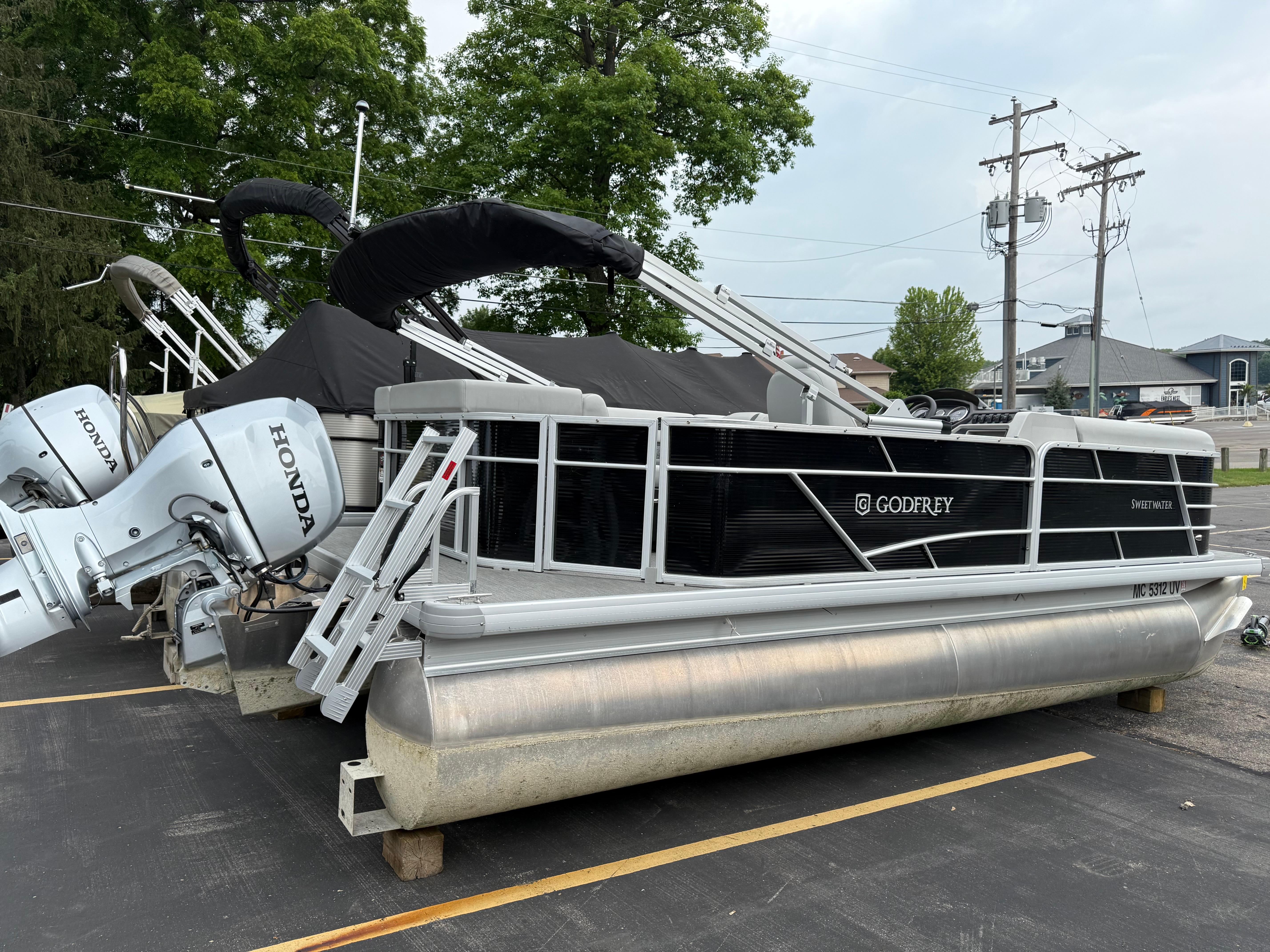 2023 Godfrey Sweetwater pontoon boat with Honda engines, parked outdoors.