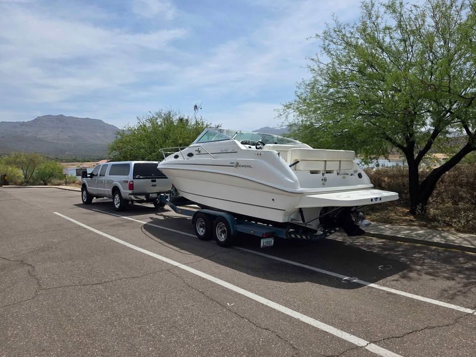 A 1997 Sea Ray 240 Sundeck on a trailer, towed by a pickup truck in a parking area.