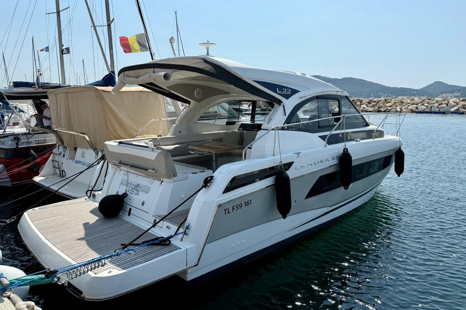 2017 Jeanneau Leader 33 yacht docked in a marina, with scenic mountain backdrop.