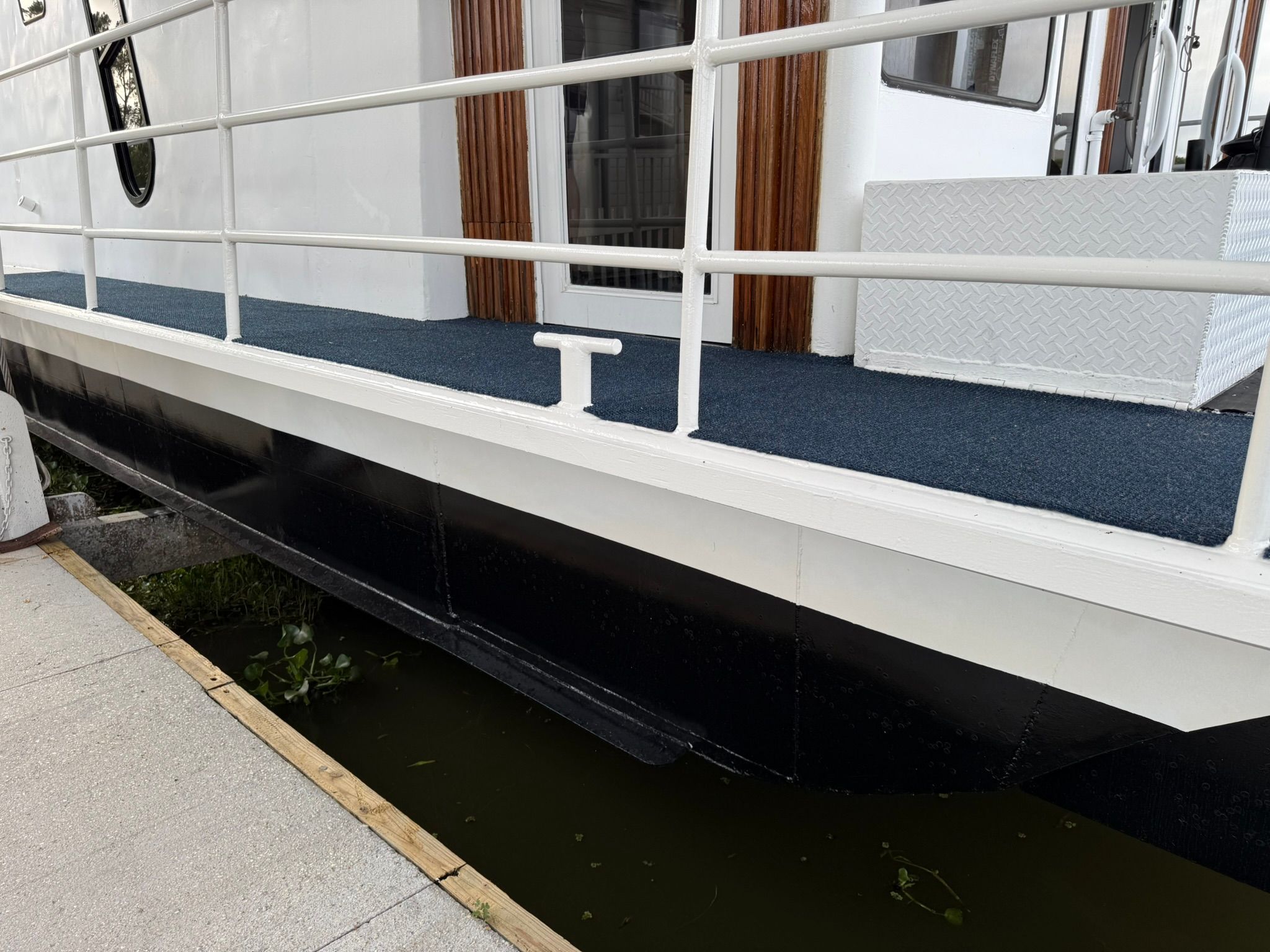 Houseboat with blue carpet and white railing at the dock.