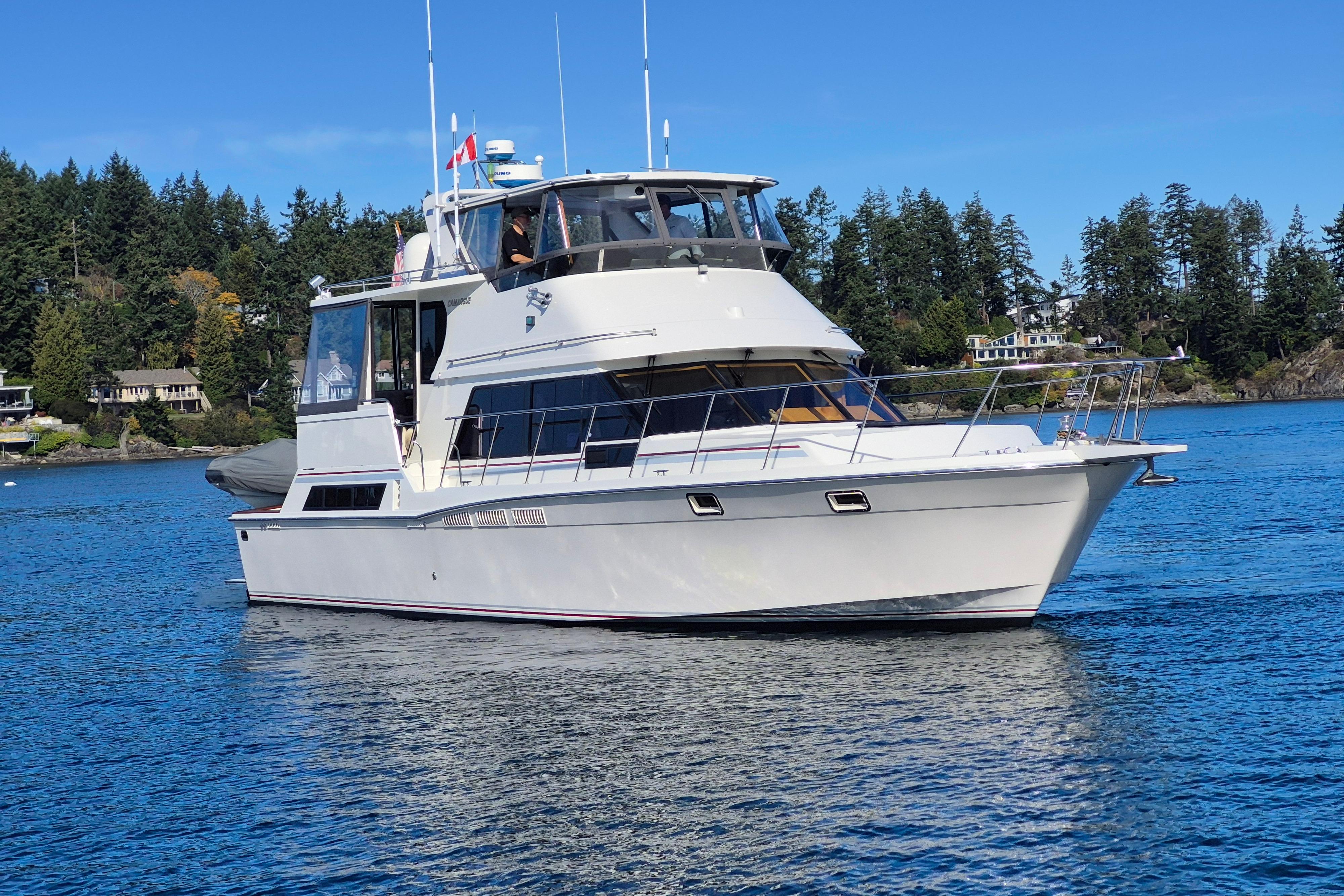 1990 Camargue 48 yacht cruising on a serene lake with forested shoreline.