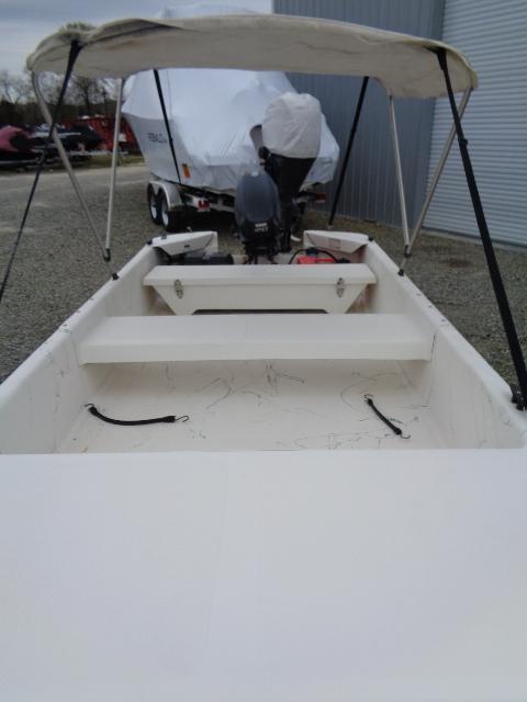 Small Sundance K14T boat with canopy, 2010 model, parked on gravel near a covered trailer.