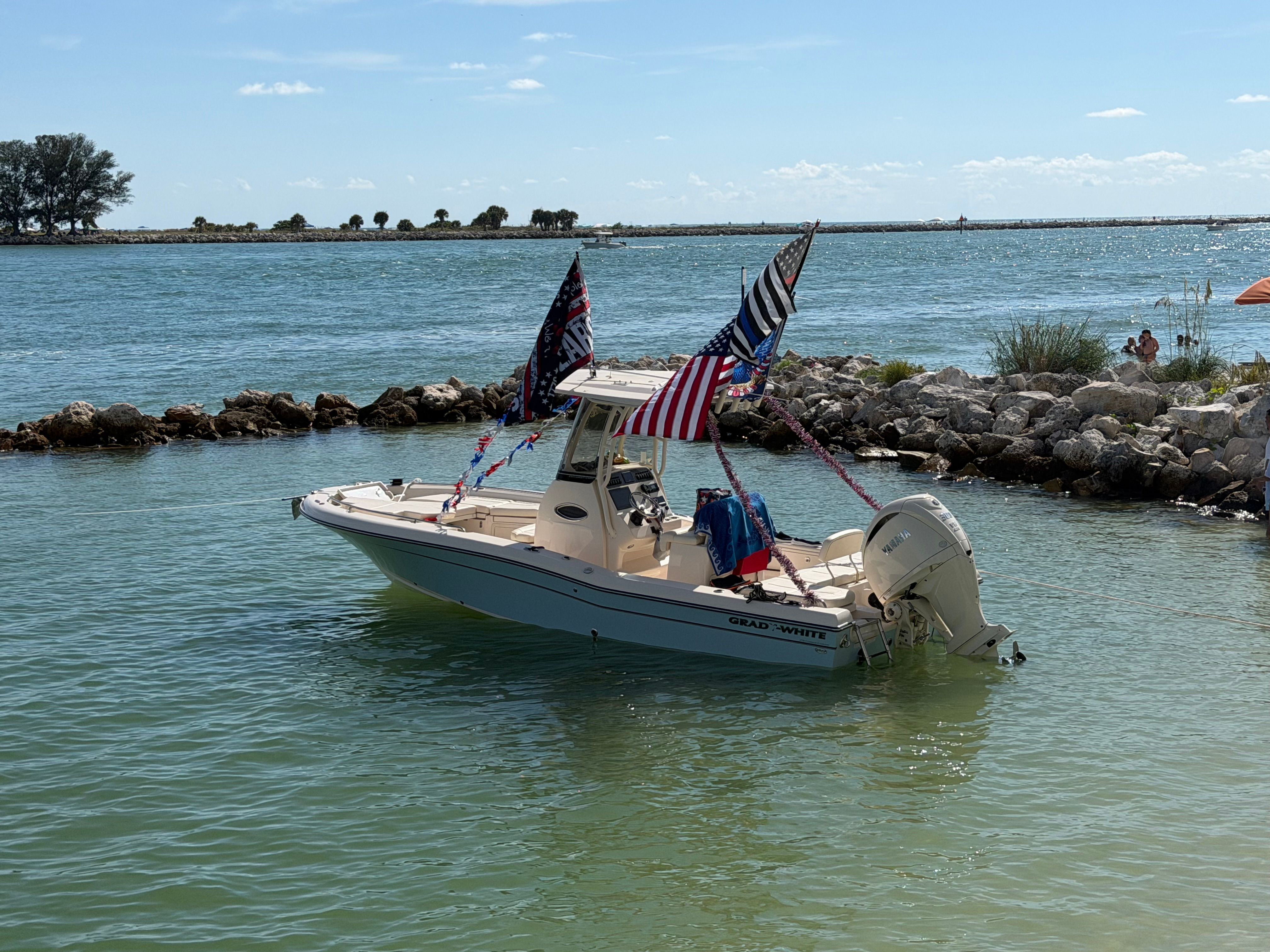 A 2024 Grady-White 251 boat floats in calm water, adorned with multiple flags.