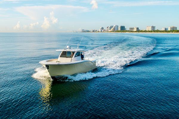 2019 Altima 38 Xcape boat cruising on calm ocean near city skyline.