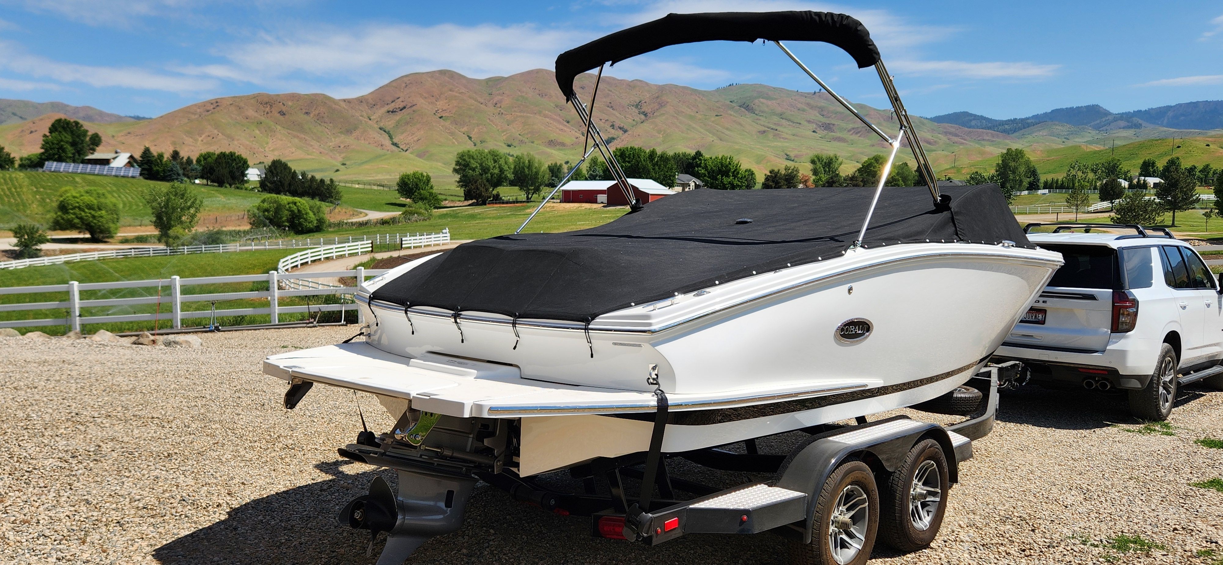 A white Cobalt CS22 boat on a trailer, surrounded by green hills and a blue sky.