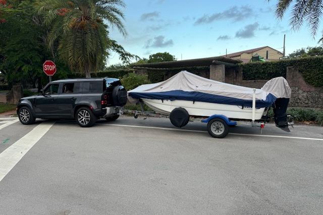 SUV towing a covered 2016 Boston Whaler 150 Montauk boat on a trailer at an intersection.