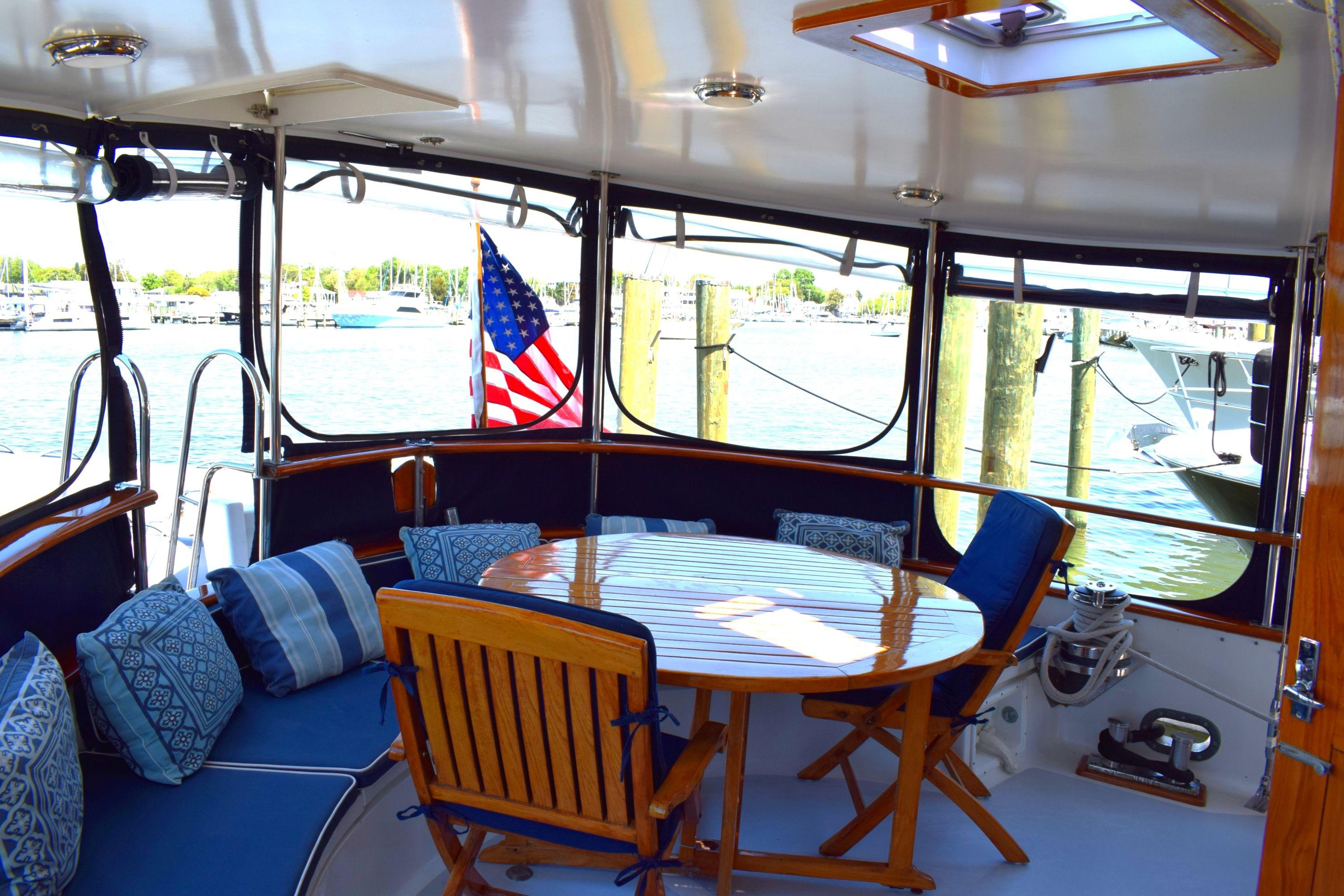 1980 Cheoy Lee 52 Motorsailer cockpit with wooden table, cushioned seating, and marina view.