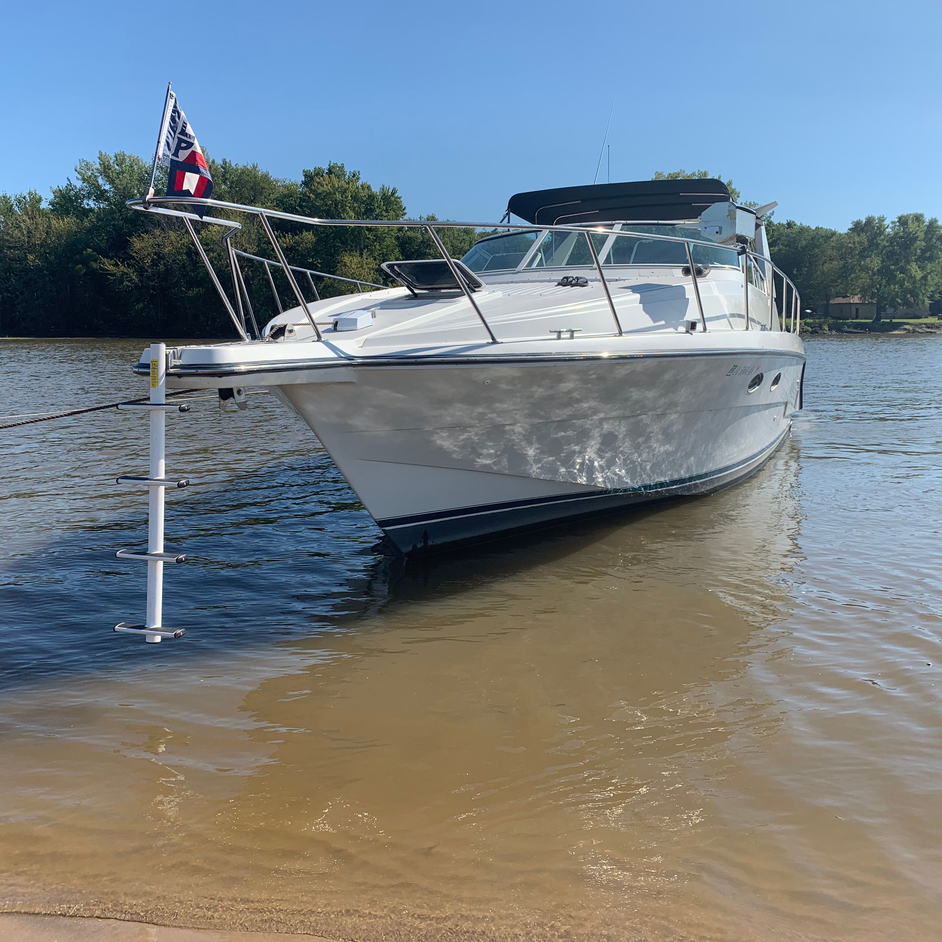 A white motorboat beached on a calm water shore, with trees in the background.