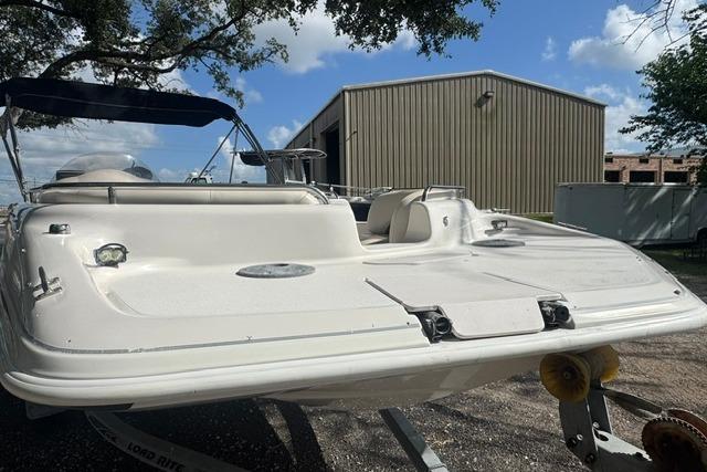 1999 Hurricane SunDeck Sport 201 OB boat on trailer, parked near a metal building.